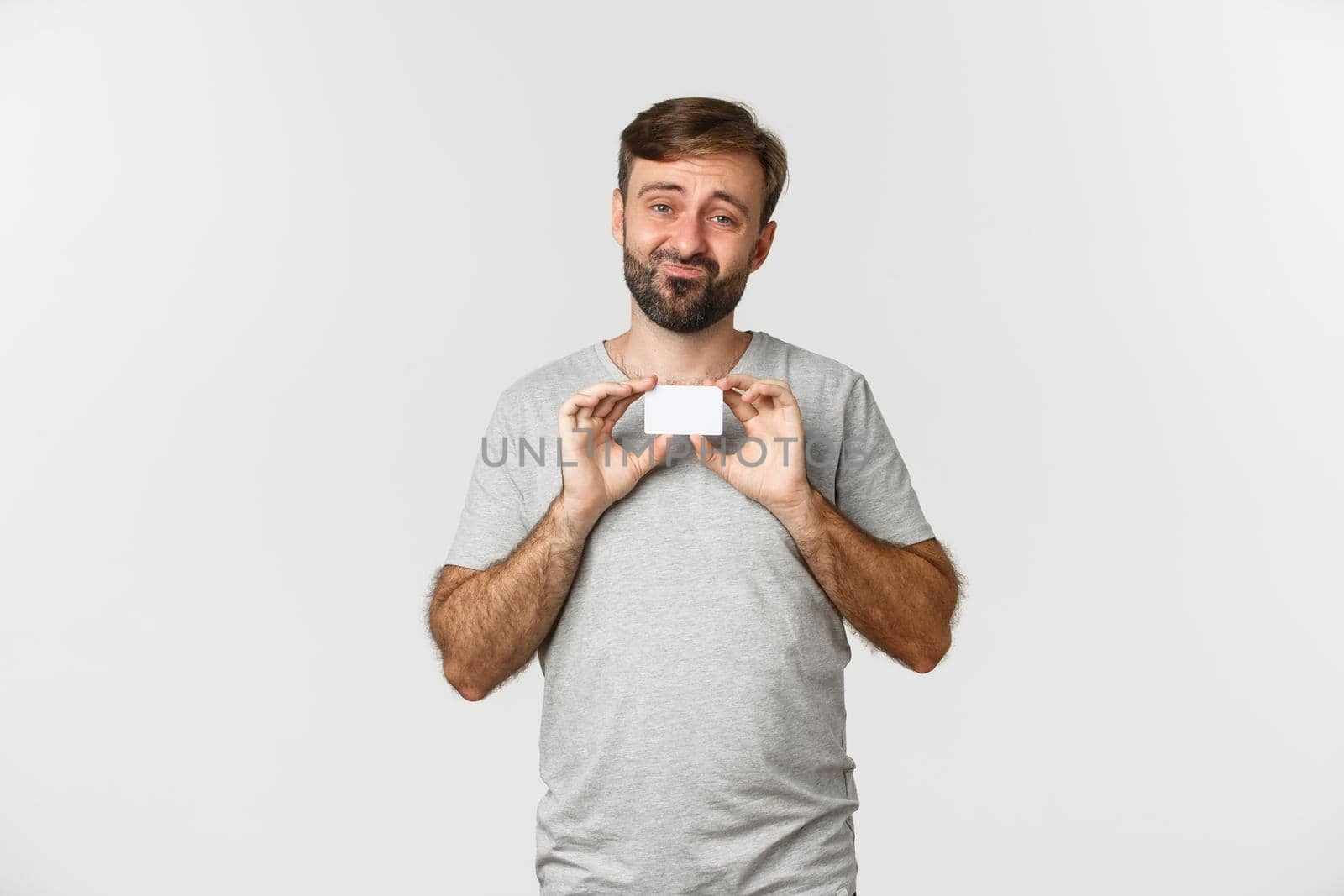 Image of gloomy guy complaining about empty bank account, showing credit card and grimacing sad, standing over white background.