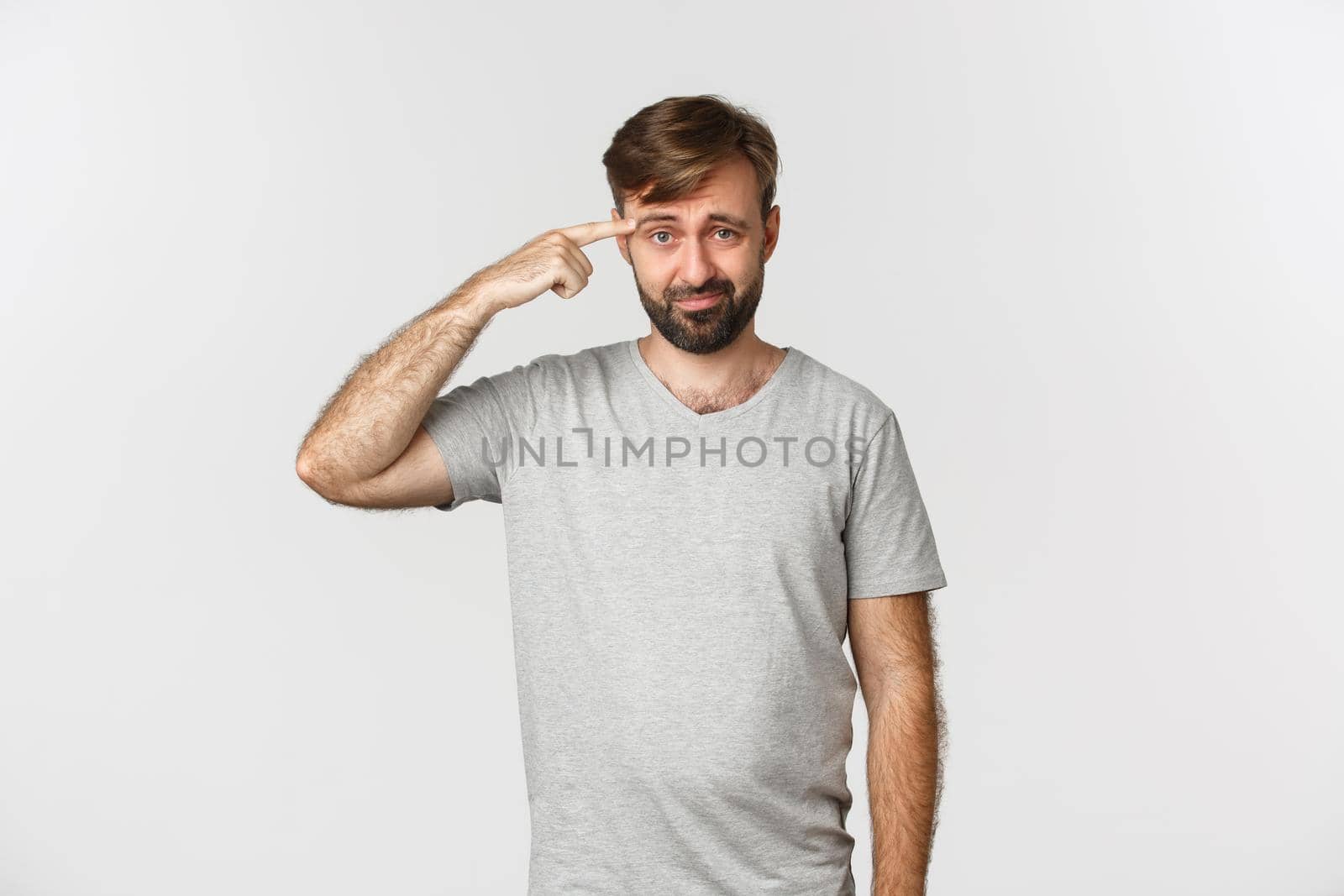 Portrait of frustrated guy scolding someone for being crazy or strange, pointing at head and frowning, standing over white background.