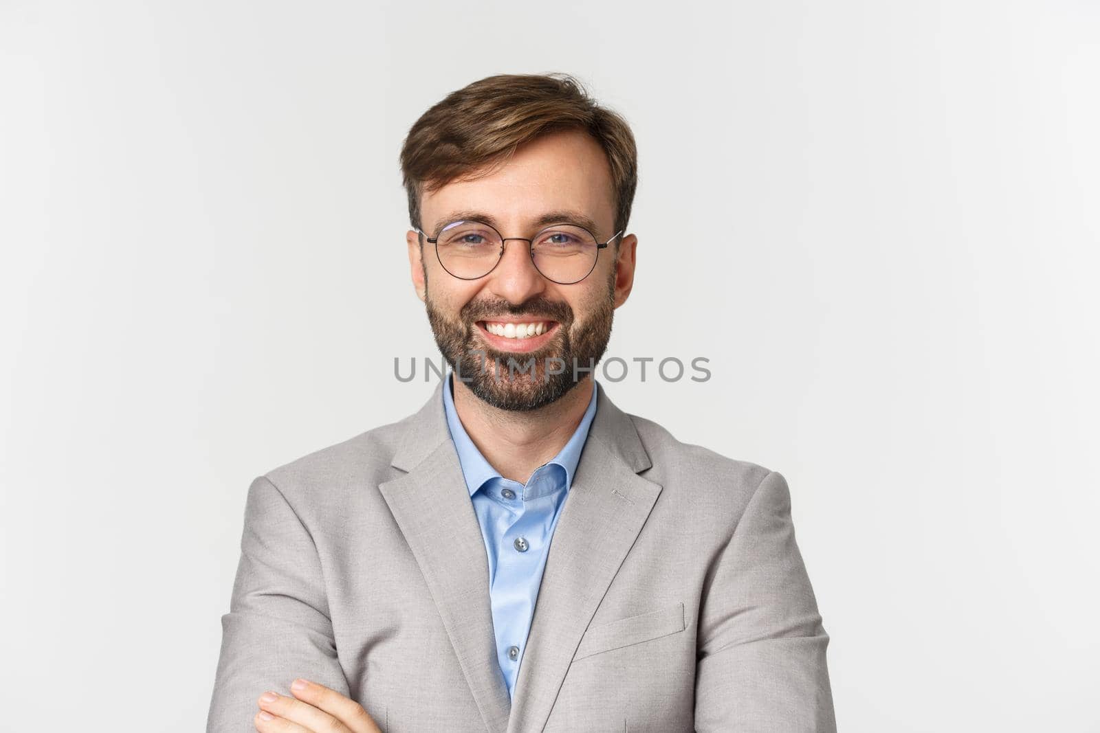 Close-up of confident handsome male bossy, wearing glasses and gray suit, cross arms on chest and smiling pleased, standing over white background.