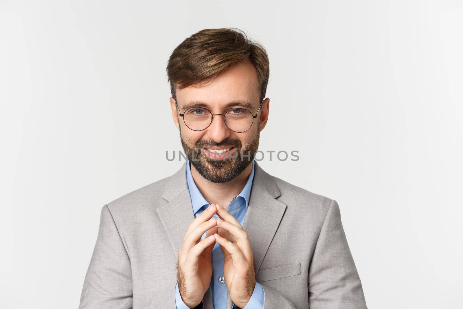 Close-up of bearded businessman in glasses and suit, scheming something, smiling devious and having perfect plan, standing over white background by Benzoix