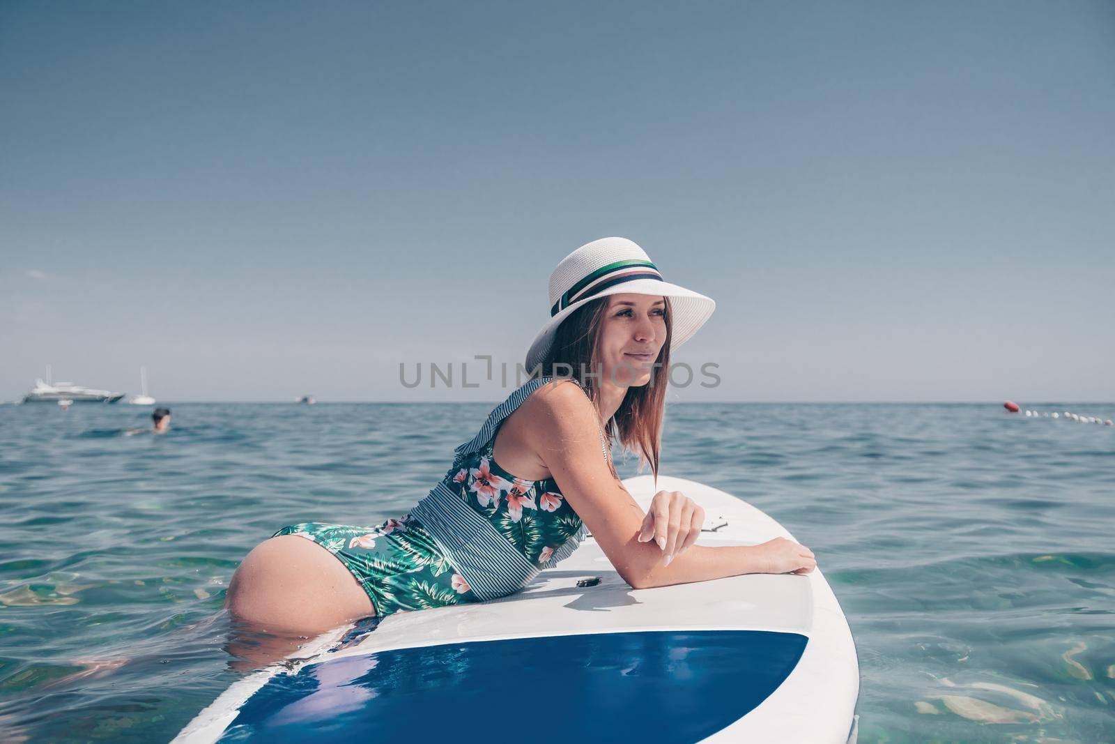 Happy young woman in swimsuits doing yoga on sup board in calm sea, early morning. Balanced pose - concept of healthy life and natural balance between body and mental development