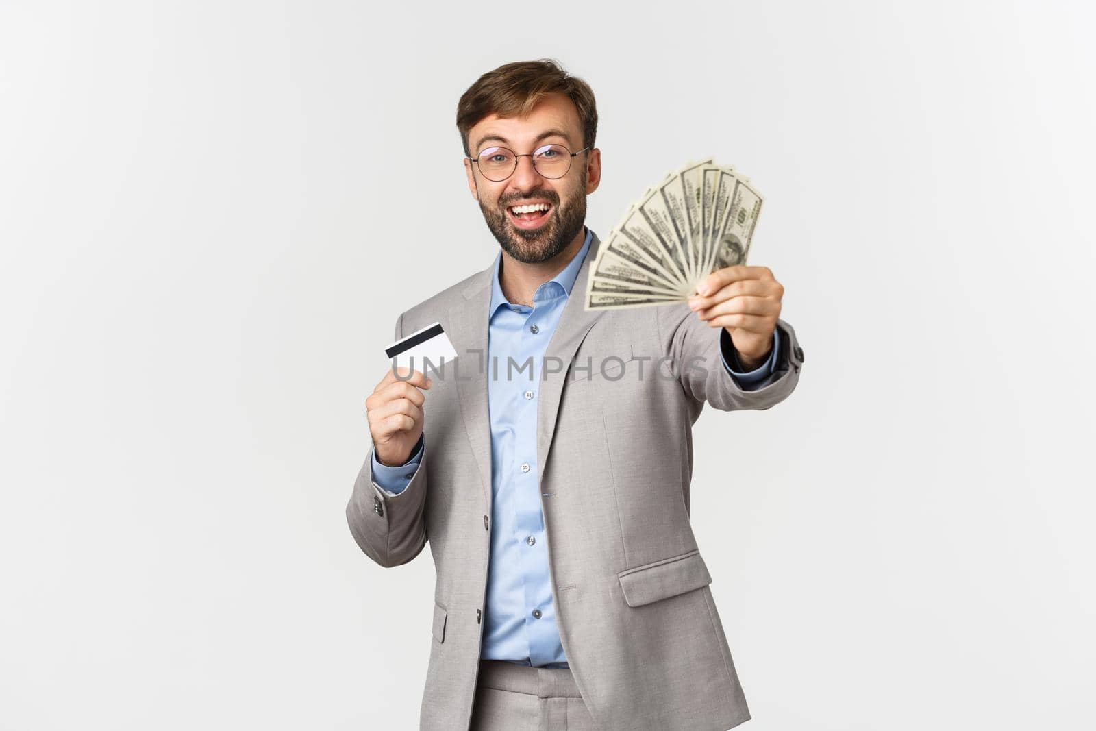 Portrait of happy successful businessman holding credit card, showing money and rejoicing, standing over white background.