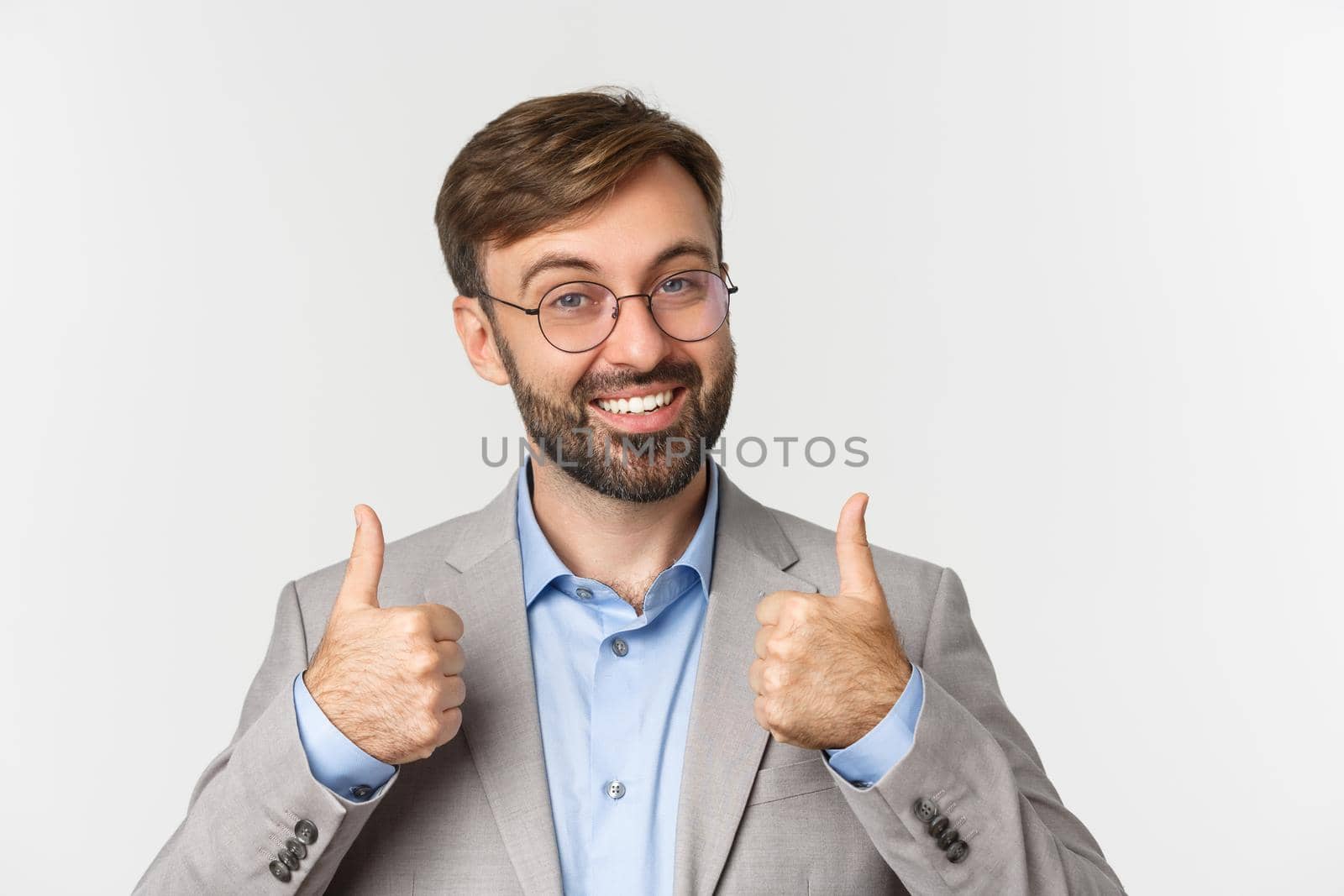 Close-up of handsome bearded man in glasses and gray suit, showing thumbs-up approval, like something, recommend product or brand, standing over white background.
