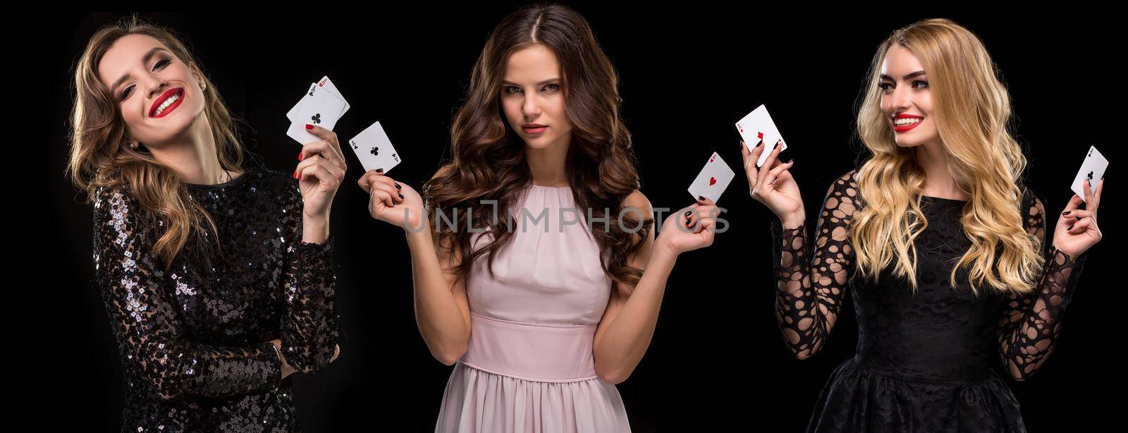 Three females in stylish dresses and jewelry. They are smiling, holding aces in their hands, posing on black background. Poker, casino. Close-up by nazarovsergey