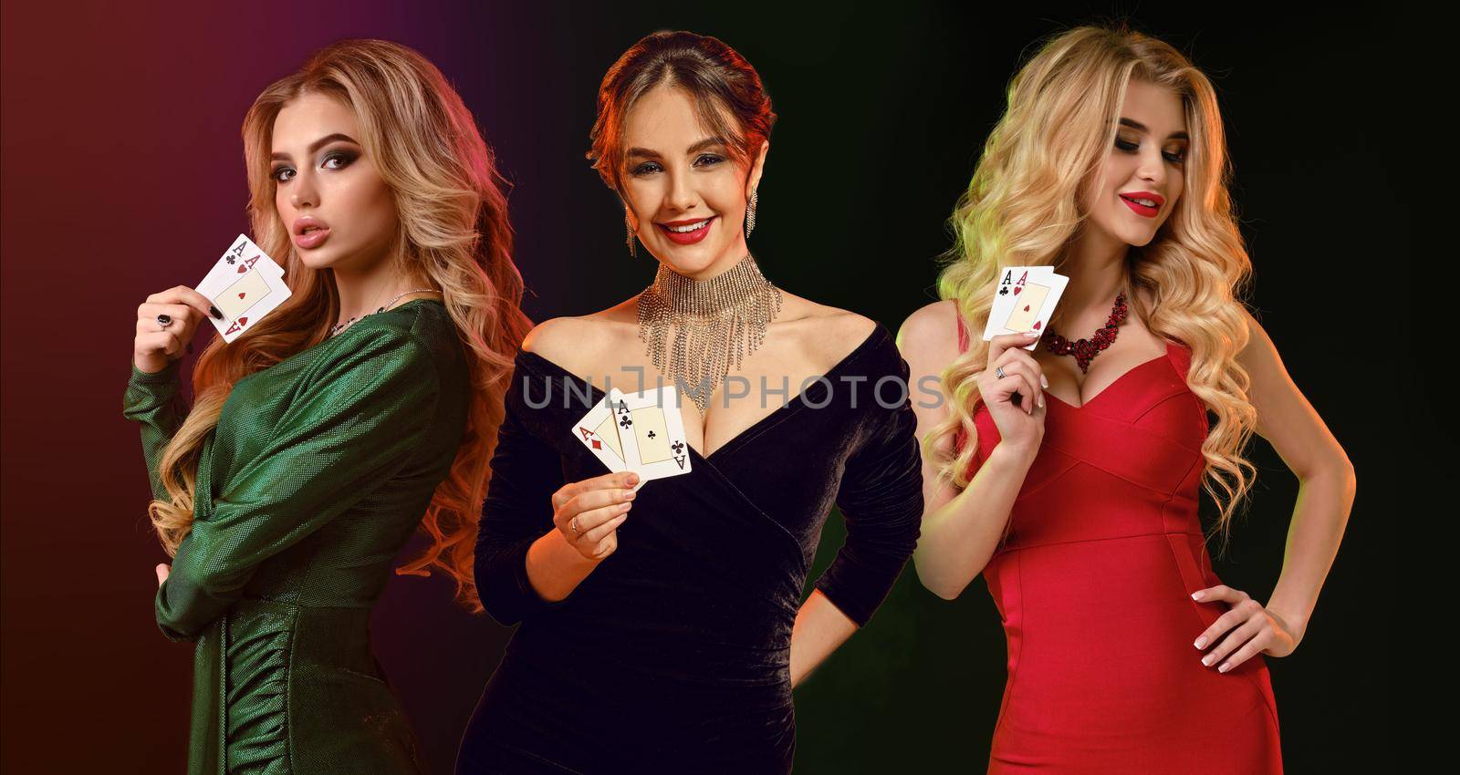 Three ladies in stylish dresses and jewelry. They smiling, showing playing cards, posing against colorful background. Poker, casino. Close-up by nazarovsergey