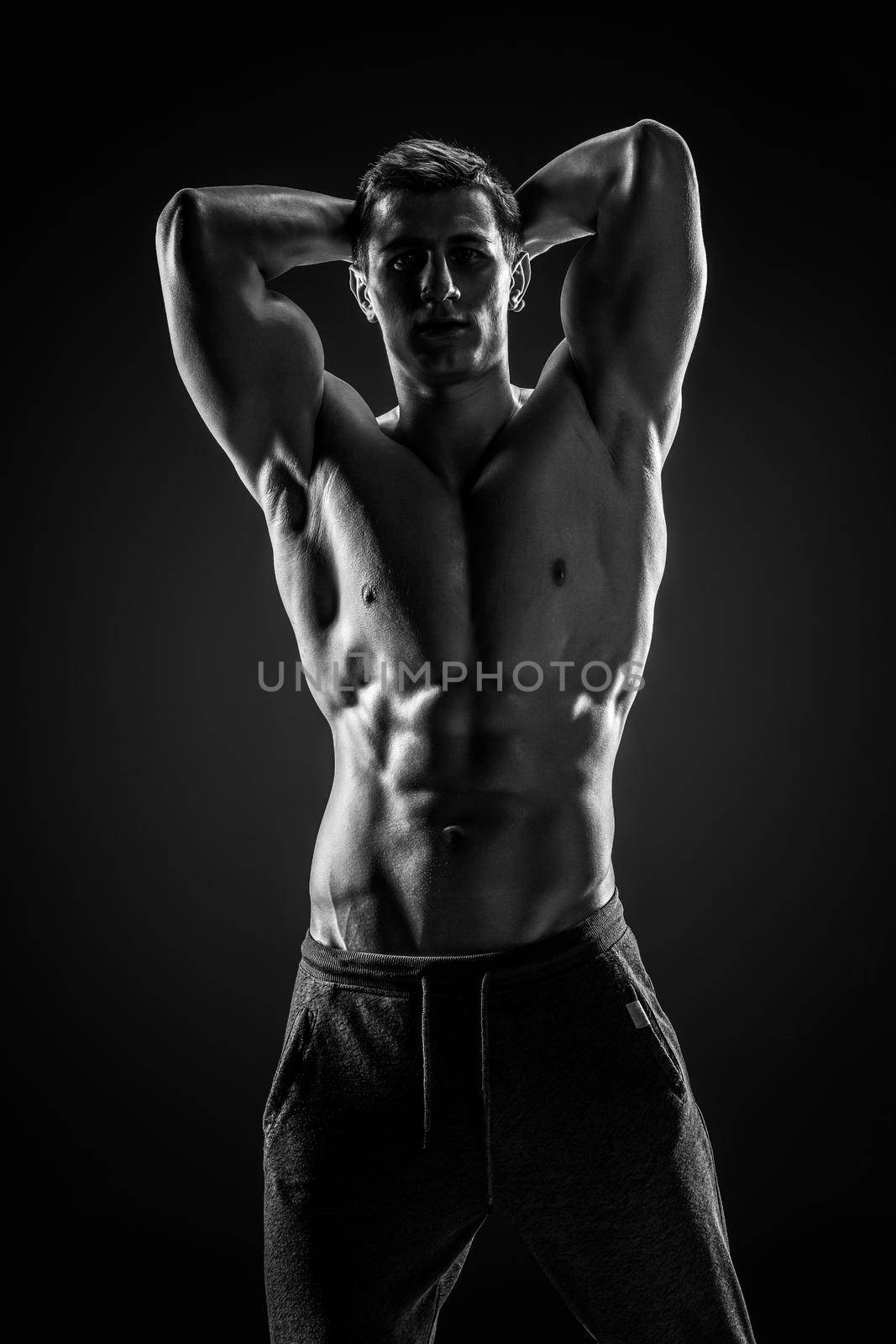 Sexy shirtless bodybuilder posing and looking at camera on black background. Extreme strength, muscles and fitness.. Black and white