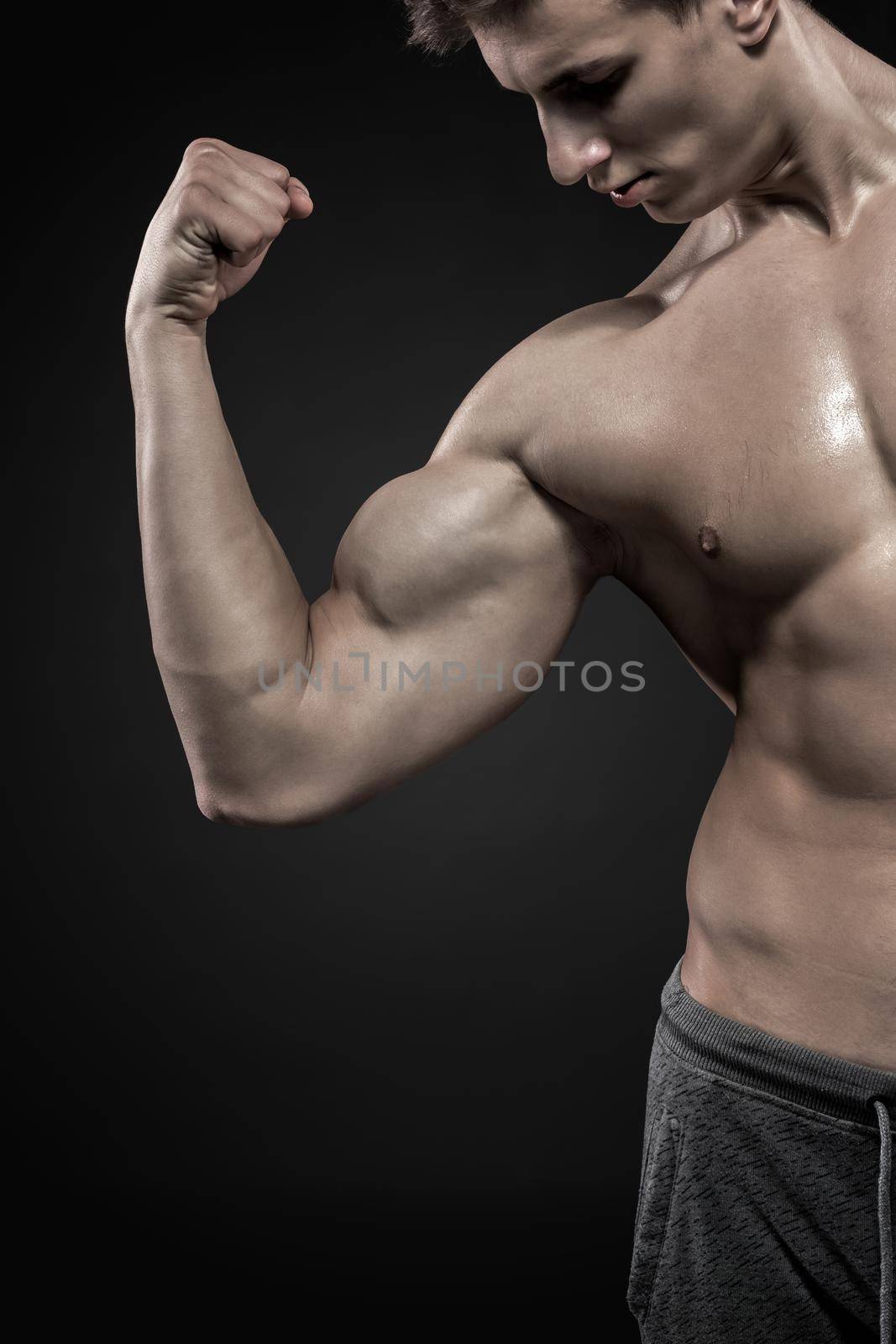 Handsome fitness man showing his triceps and biceps muscles on black background