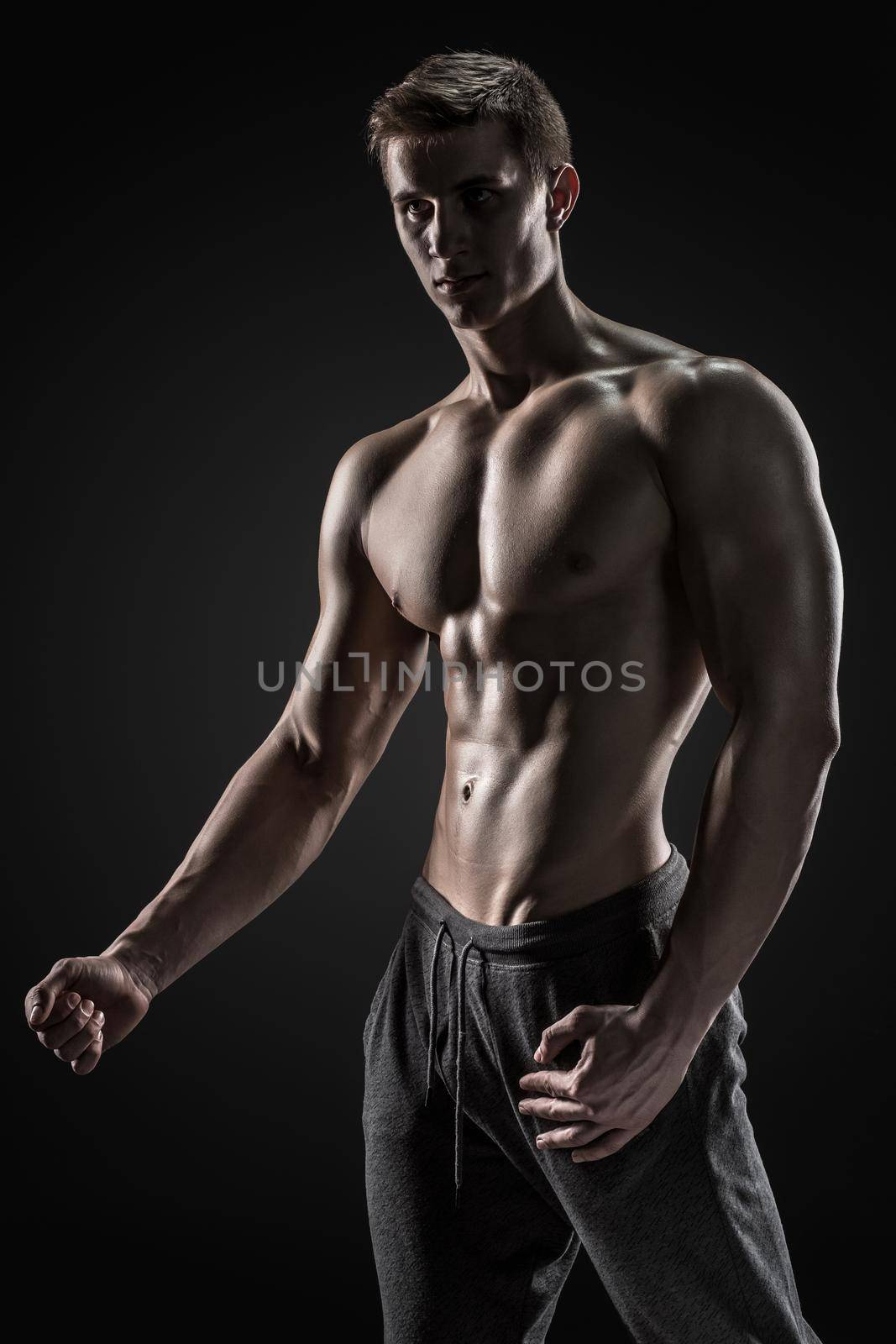 Sexy shirtless bodybuilder posing and looking at camera on black background. Extreme strength, muscles and fitness.