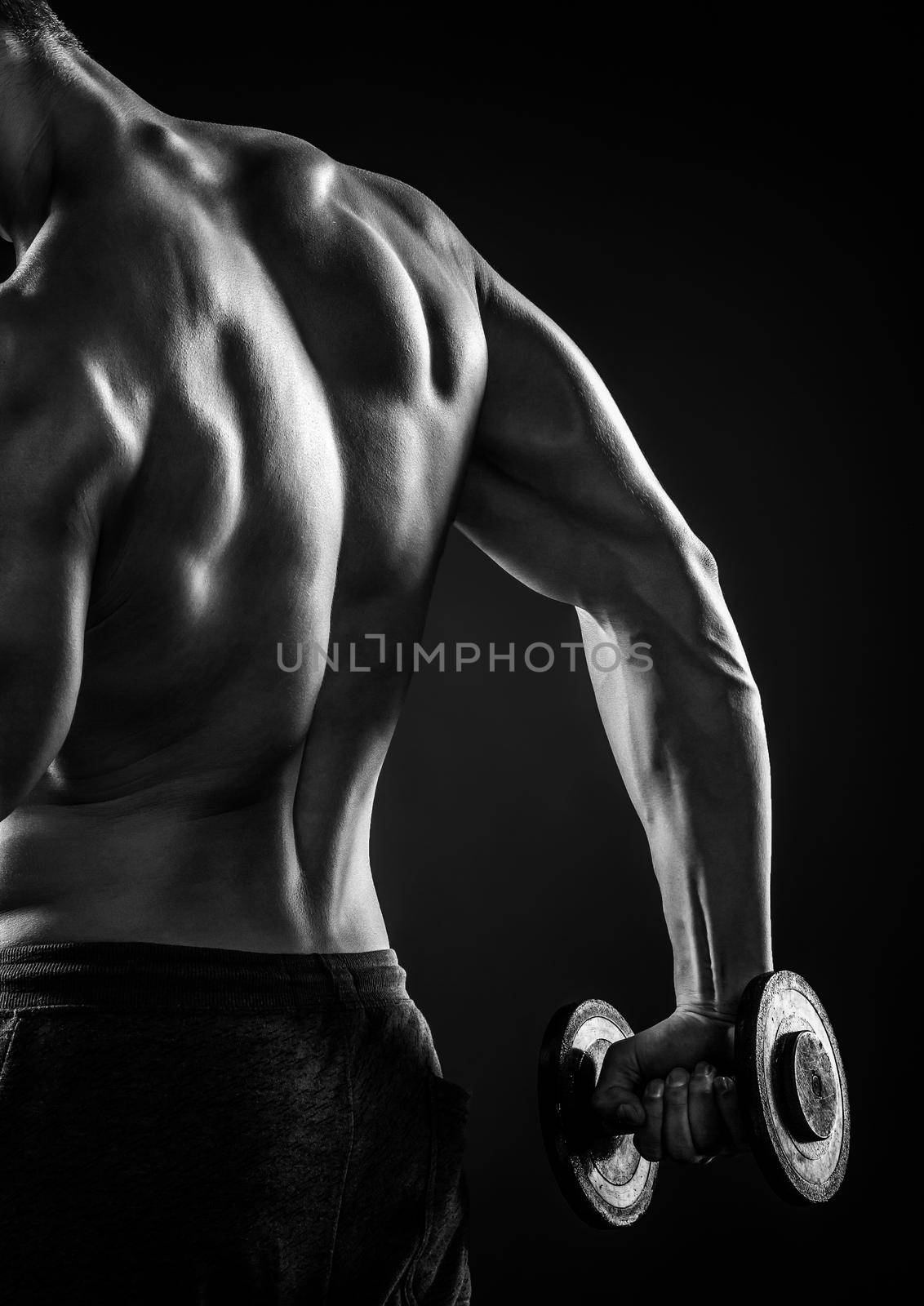 Muscular fitness man with dumbbells on black background, rear view. Close-up. Black and white