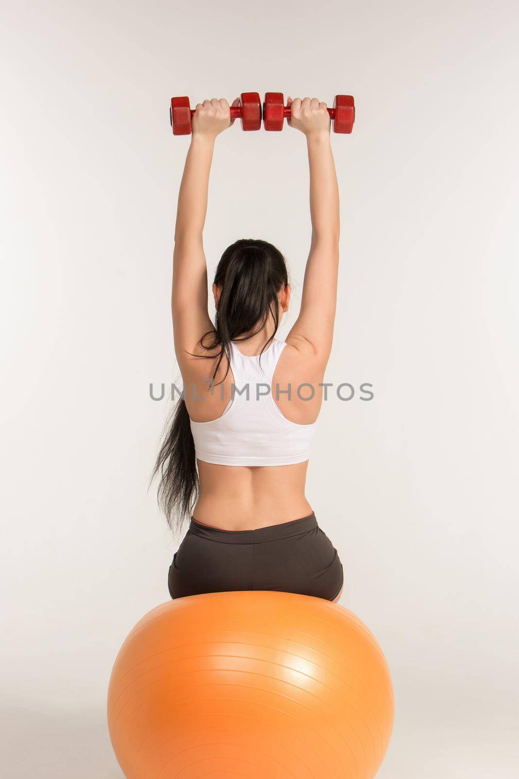 Young beautiful sportswoman doing fitness exercise with dumbbells on pilates ball, at studio shot. Health, beauty and fitness concept.