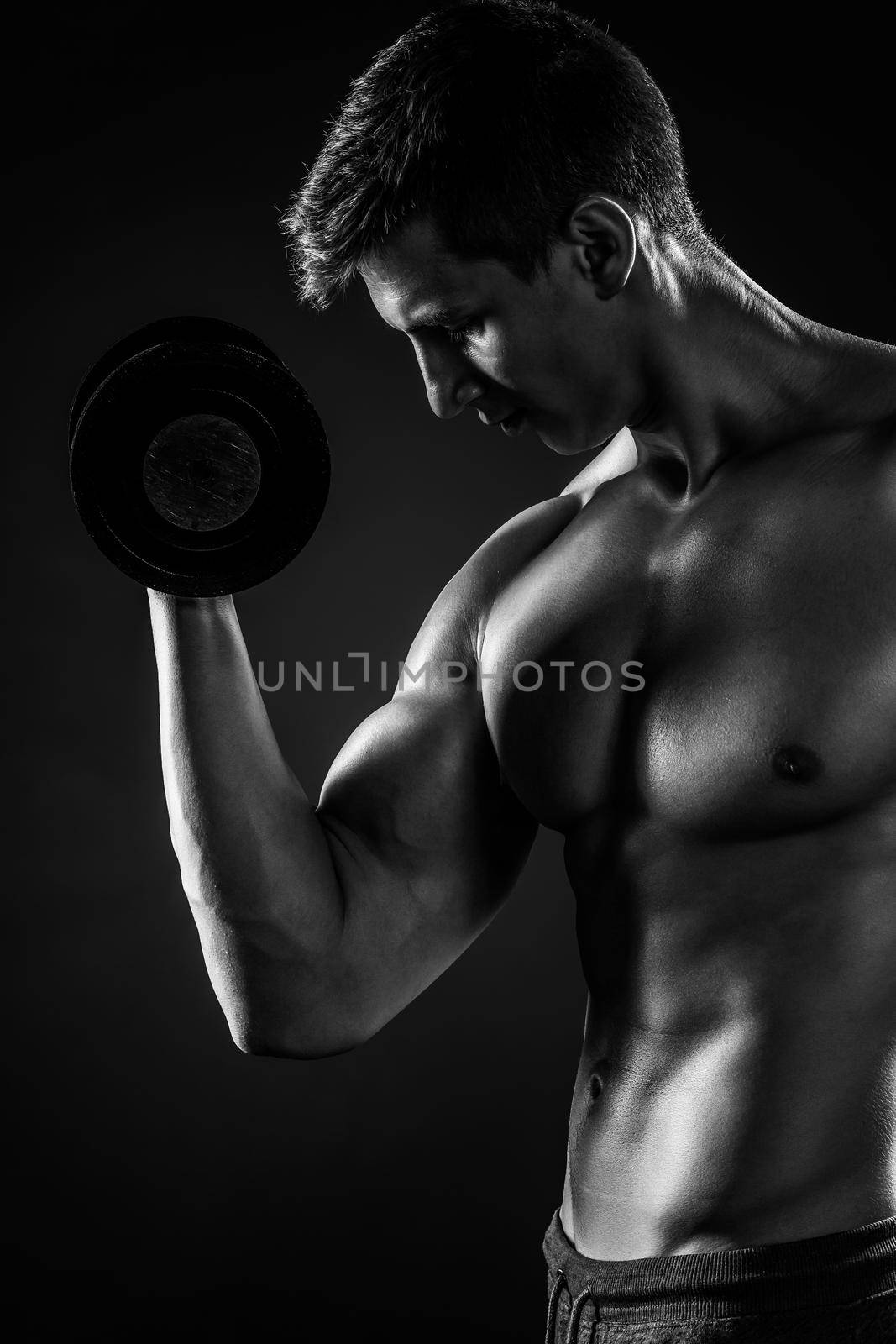 Muscular man working out doing exercises with dumbbells at biceps on black background. Close-up. Black and white