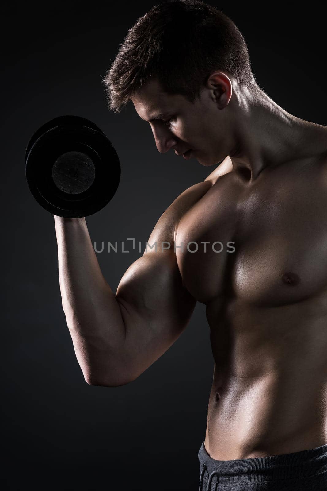 Muscular man working out doing exercises with dumbbells at biceps on black background. Close-up