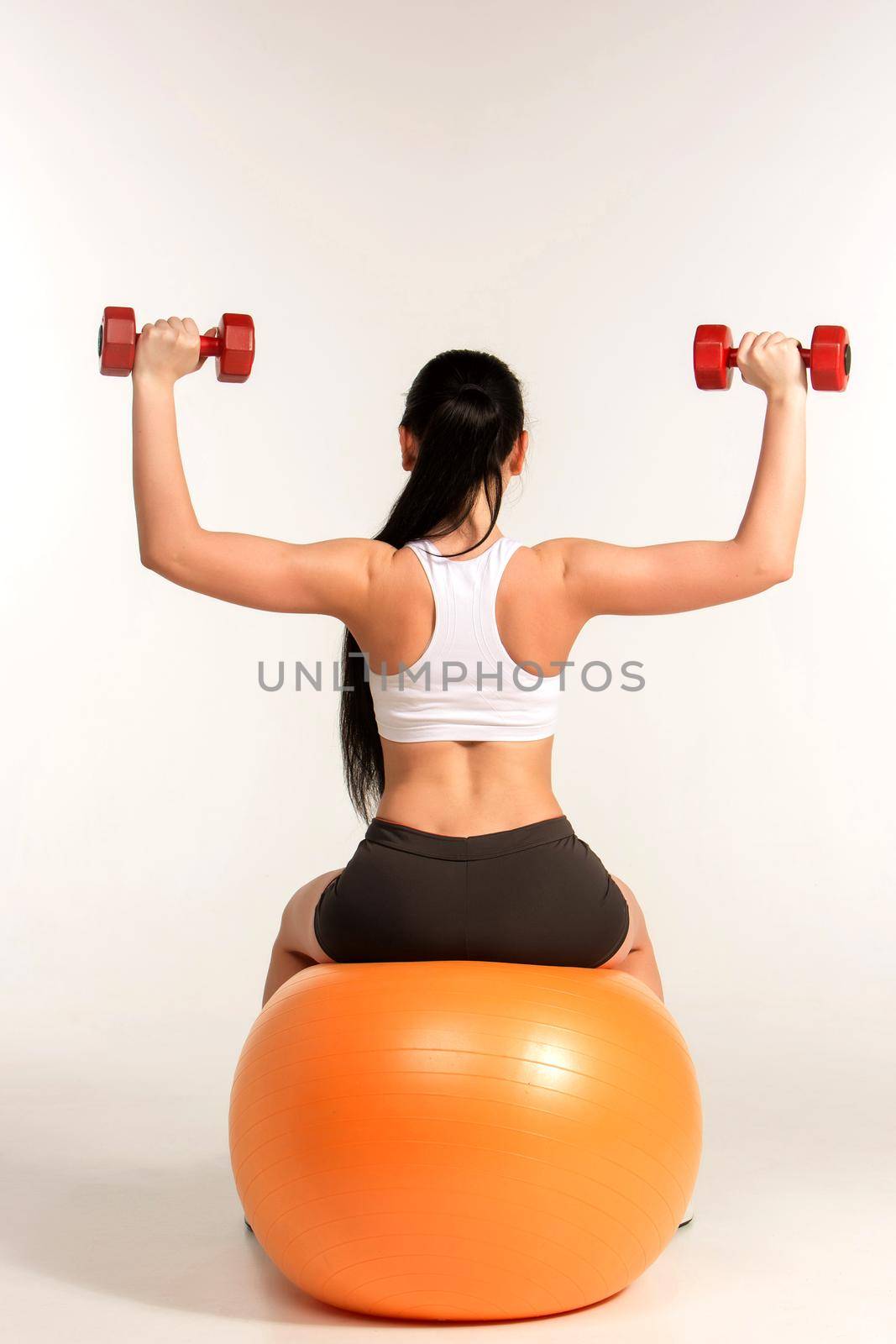 Young beautiful sportswoman doing fitness exercise with dumbbells on pilates ball, at studio shot. Health, beauty and fitness concept.