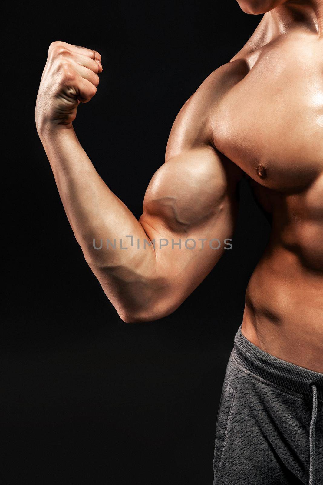 Image of very muscular man posing with naked torso in studio and looking behind on black background. Close up