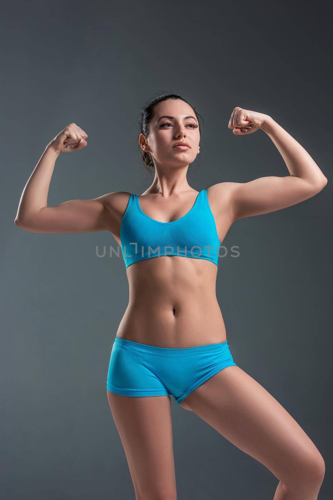 Muscular young woman athlete standing looking to the right. Raise your hands up. It shows strength