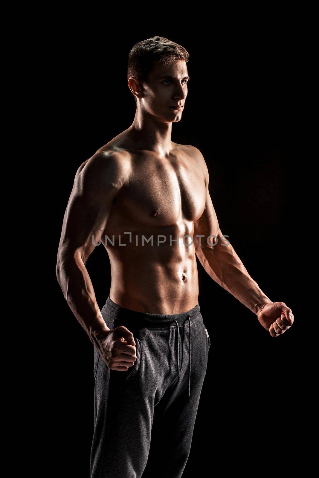 Sexy muscular man posing with naked torso in studio and looking behind on black background.