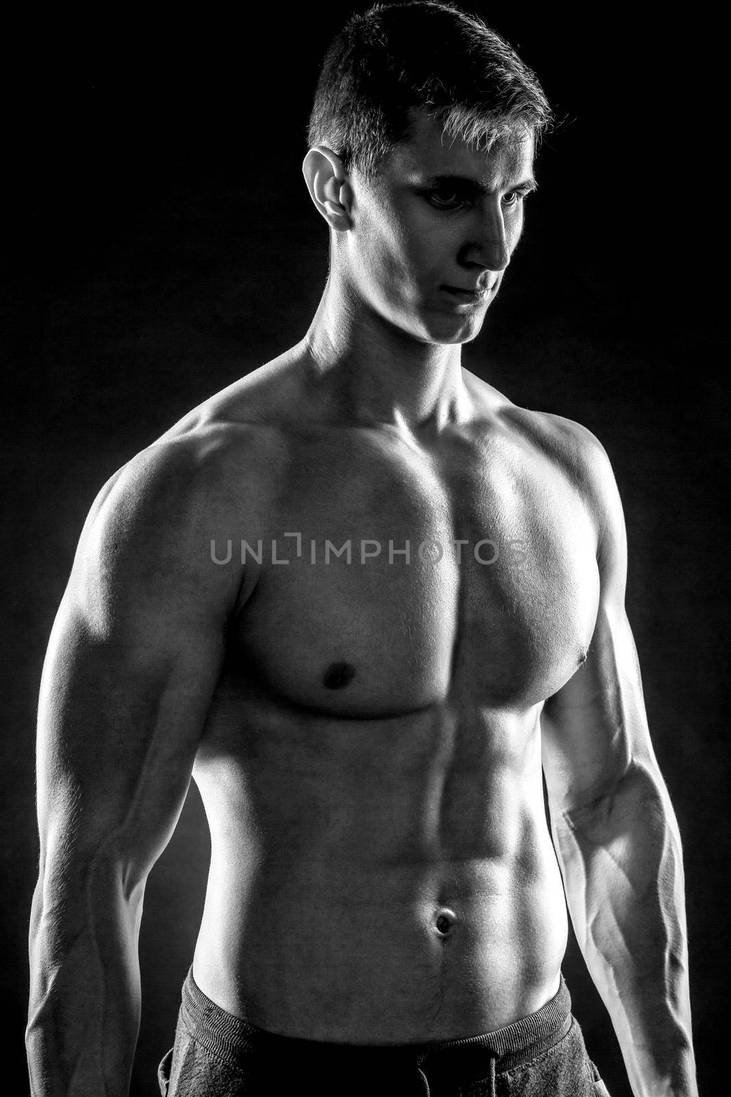 Mighty fitness man showing his gread body with dumbbells in hand on black background. Black and white. Close up