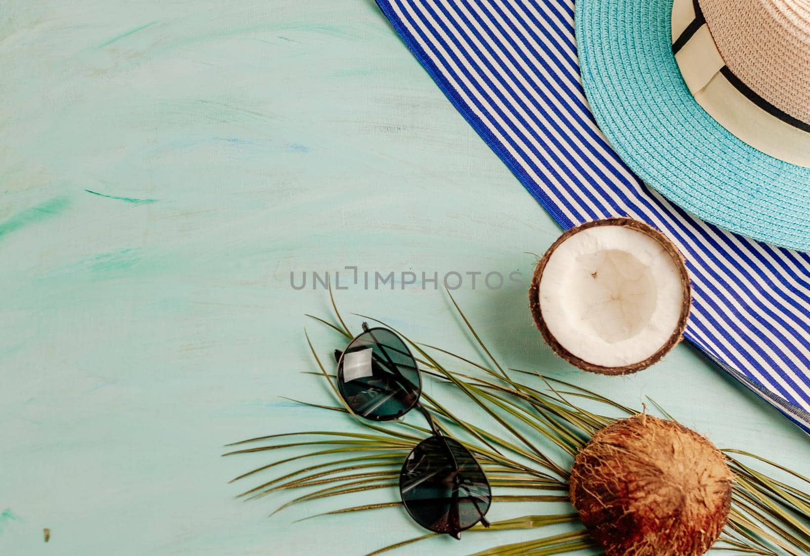 Summer composition or layout. Tropical palm leaves, hat, glasses, beach towel, coconut on a background of sea greens. The concept of the summer season and heat. Flat lay, top view, copy space