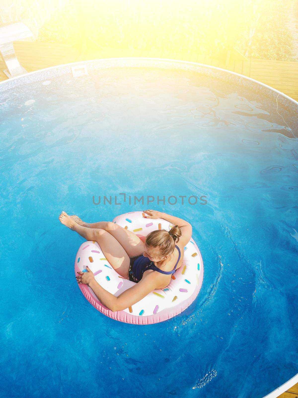 Summer warm vacation.The girl sits on a rubber ring in the form of donut in blue pool in the sun.Time to relax on an air mattress. Having fun in the water for a family vacation.Sea resort.Copy space.