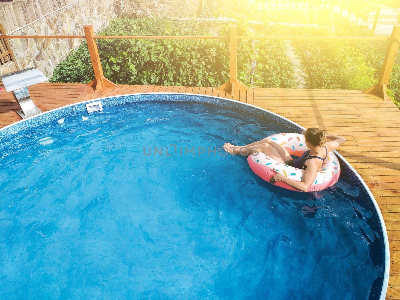 Summer warm vacation.The girl sits on a rubber ring in the form of donut in blue pool in the sun.Time to relax on an air mattress. Having fun in the water for a family vacation.Sea resort.Copy space.