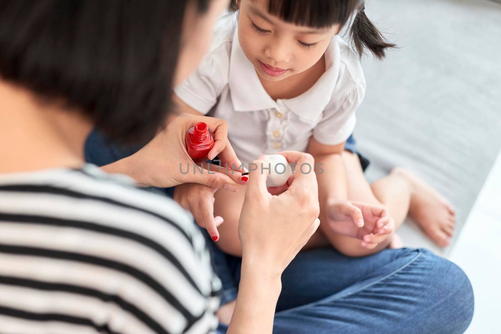 Beautiful young mother is painting the nail varnish to her cute little daughter