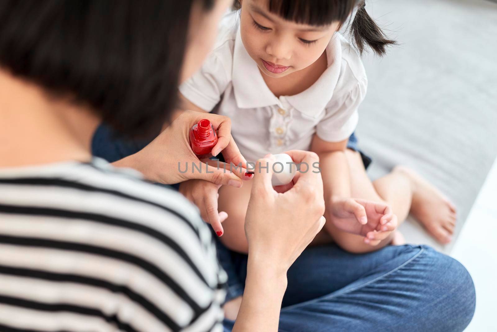 Beautiful young mother is painting the nail varnish to her cute little daughter by makidotvn