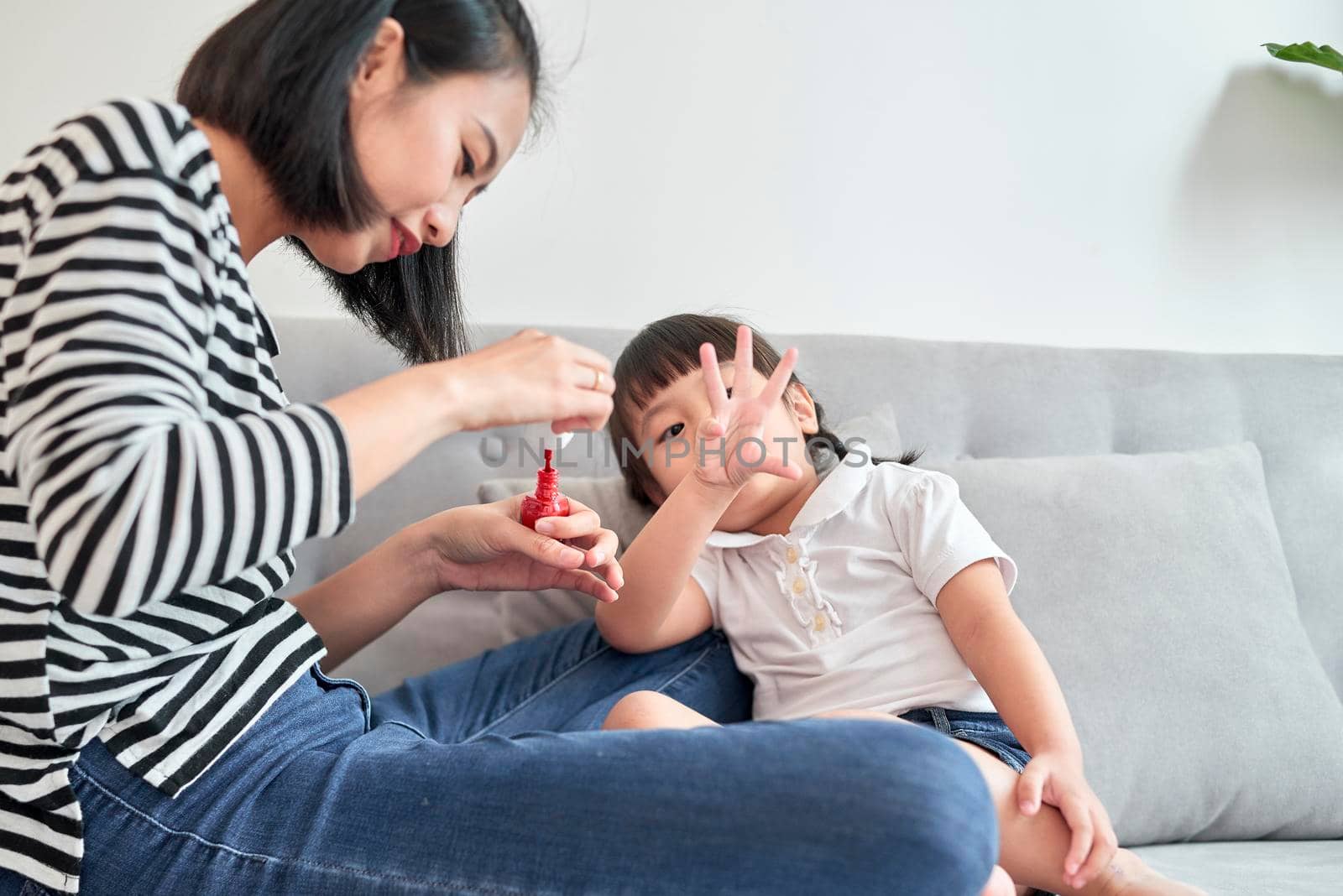 Beautiful young mother is painting the nail varnish to her cute little daughter