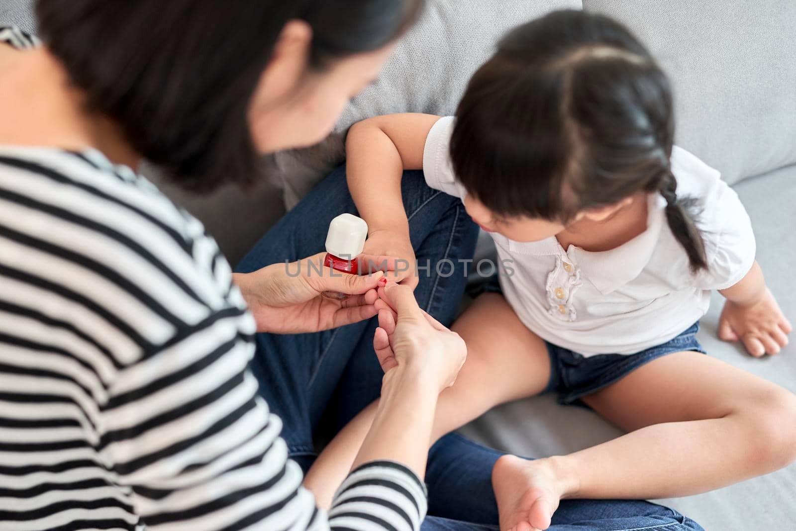 Beautiful young mother is painting the nail varnish to her cute little daughter by makidotvn