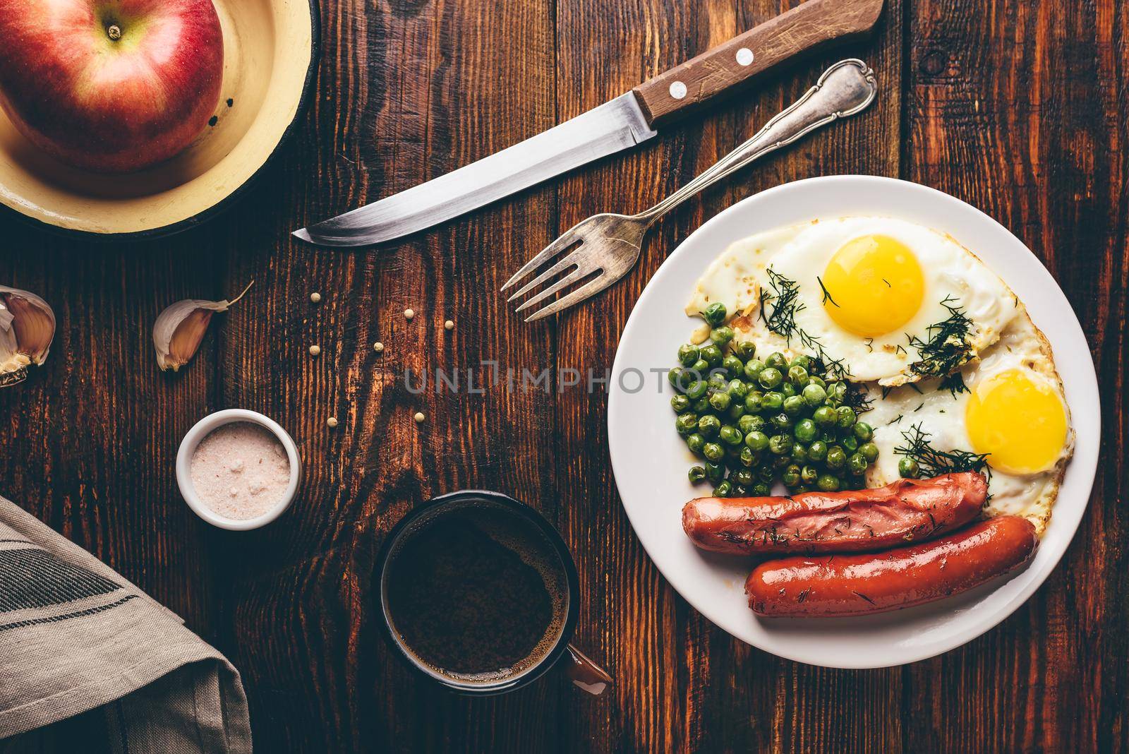 Breakfast with fried eggs, sausages and green peas on white plate