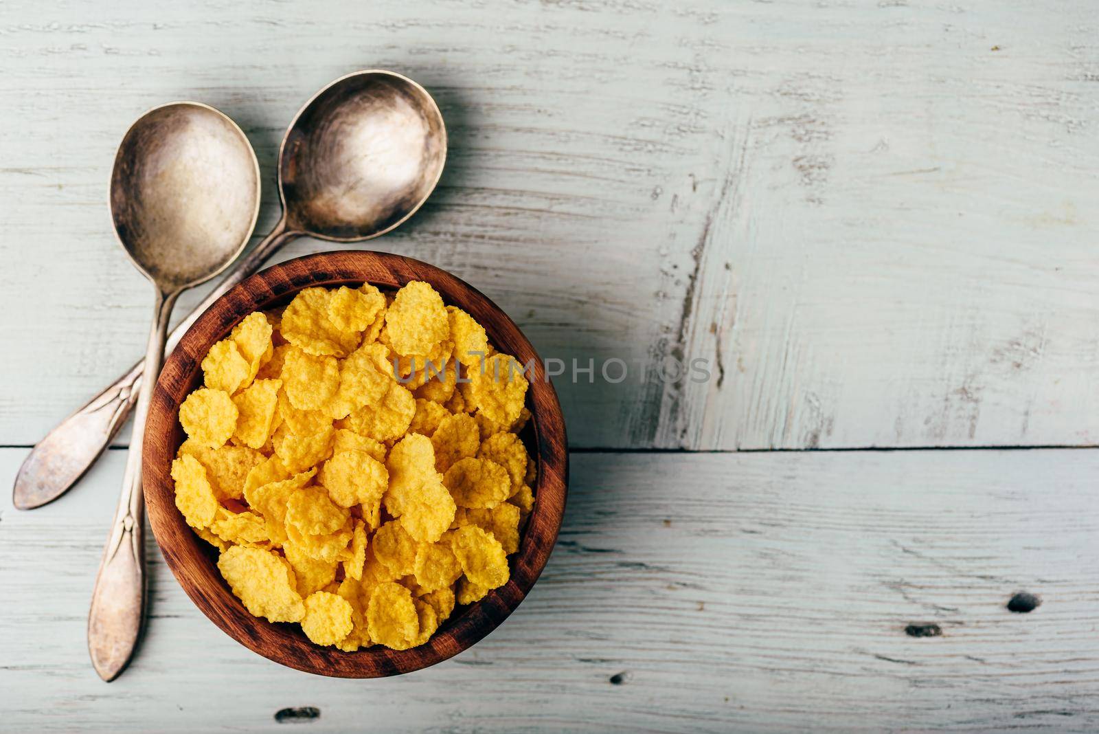 Rustic bowl of corn flakes with spoons on a wooden surface