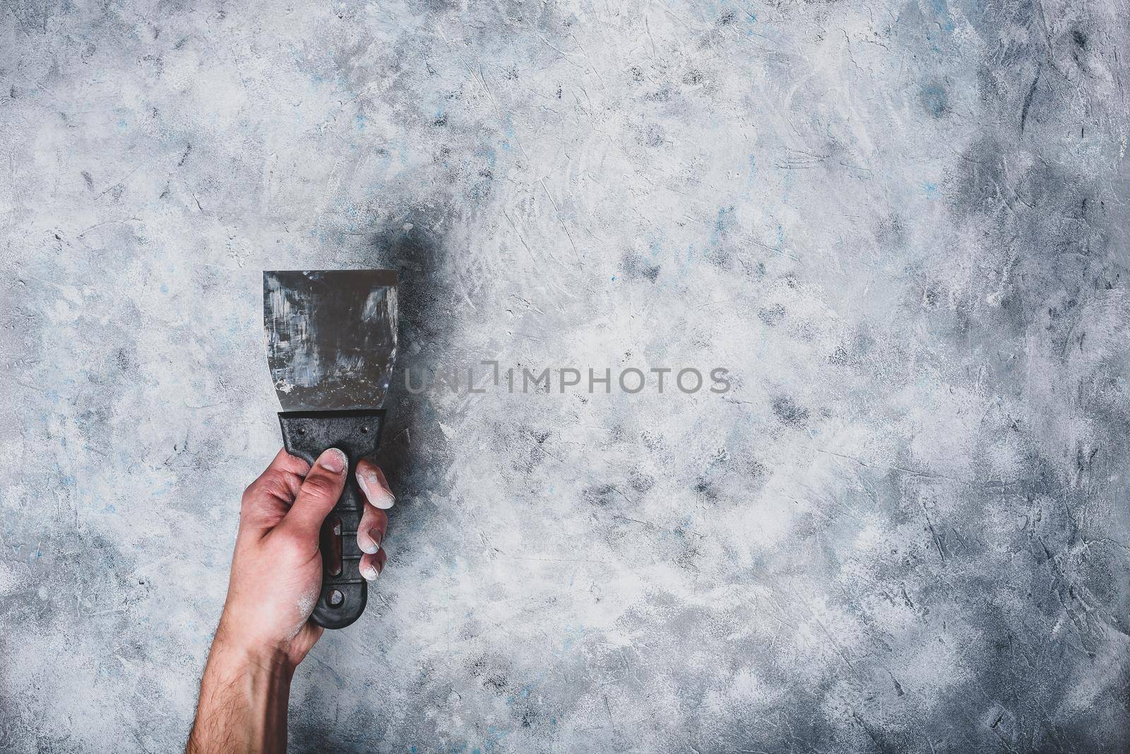 Hand holds dirty spatula. Gray concrete wall background.