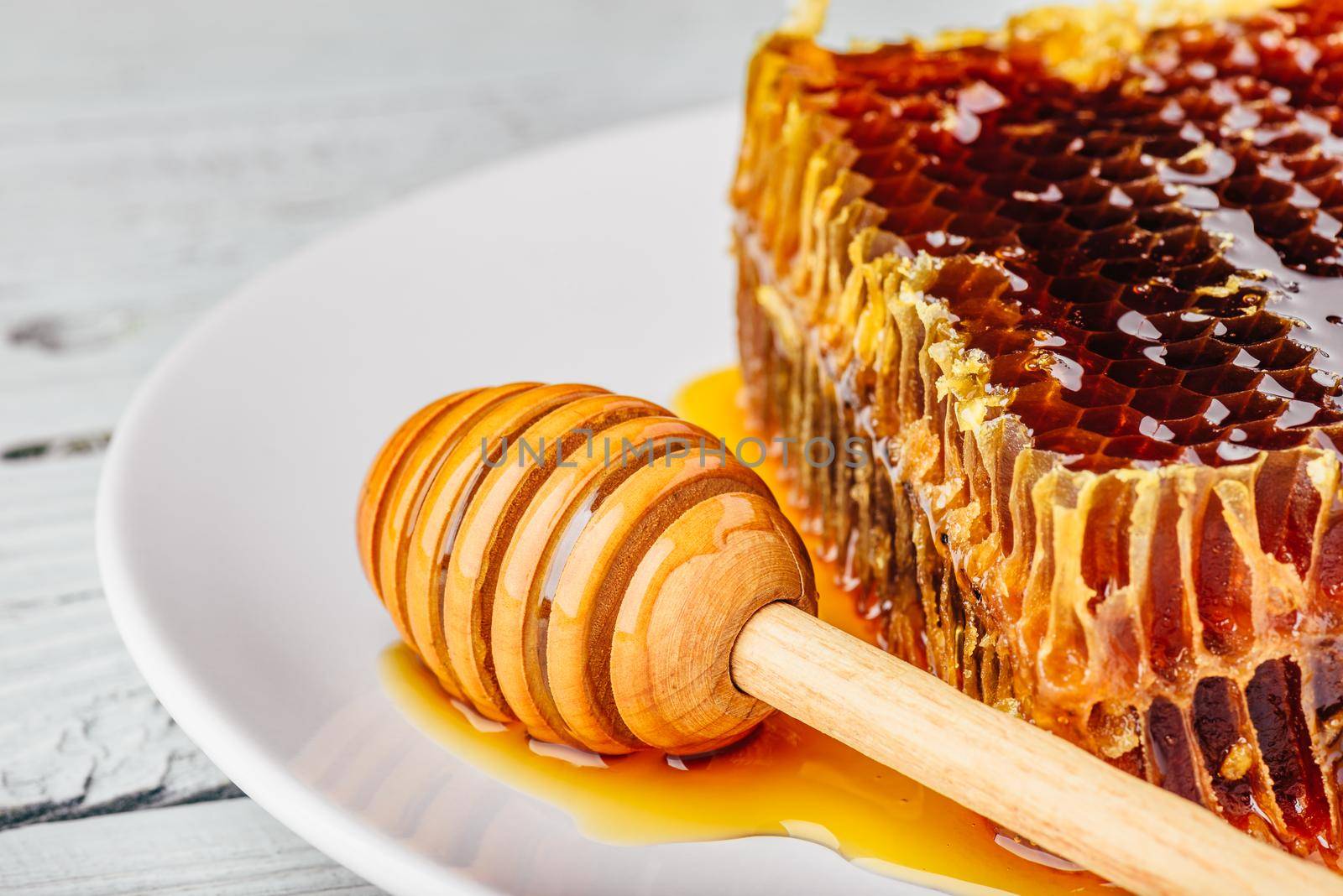 Delicious honeycomb on white plate with wooden honey dipper