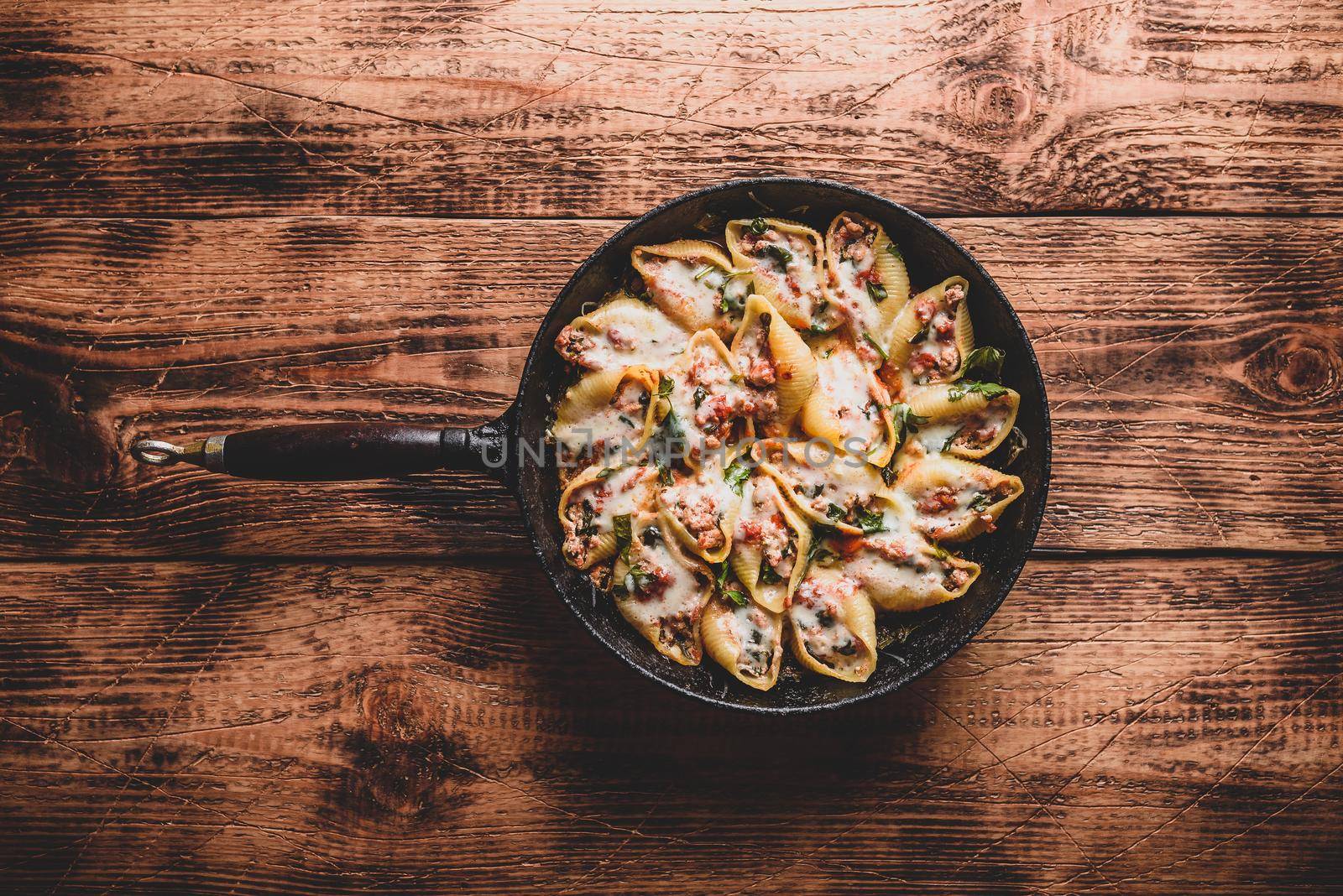 Skillet of baked jumbo shells pasta stuffed with ground beef, spinach and cheese