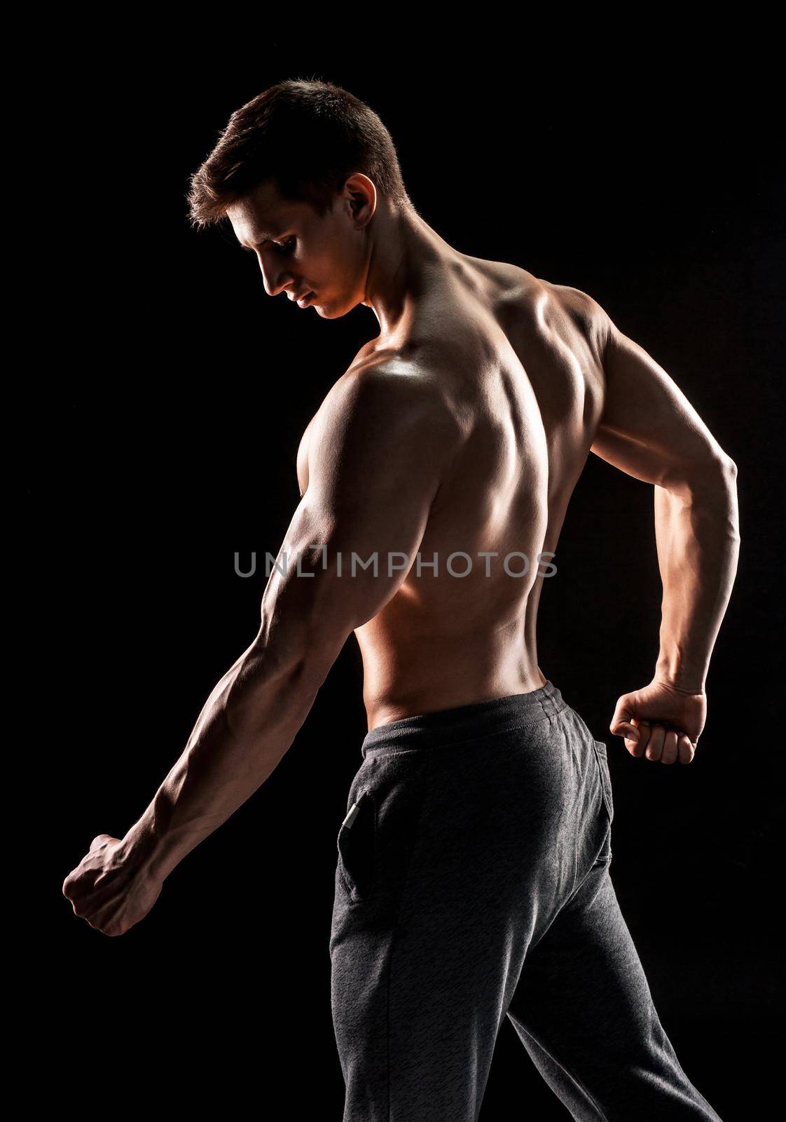 Strong bodybuilder man posing with perfect abs, houlders,biceps, triceps and chest on black background.