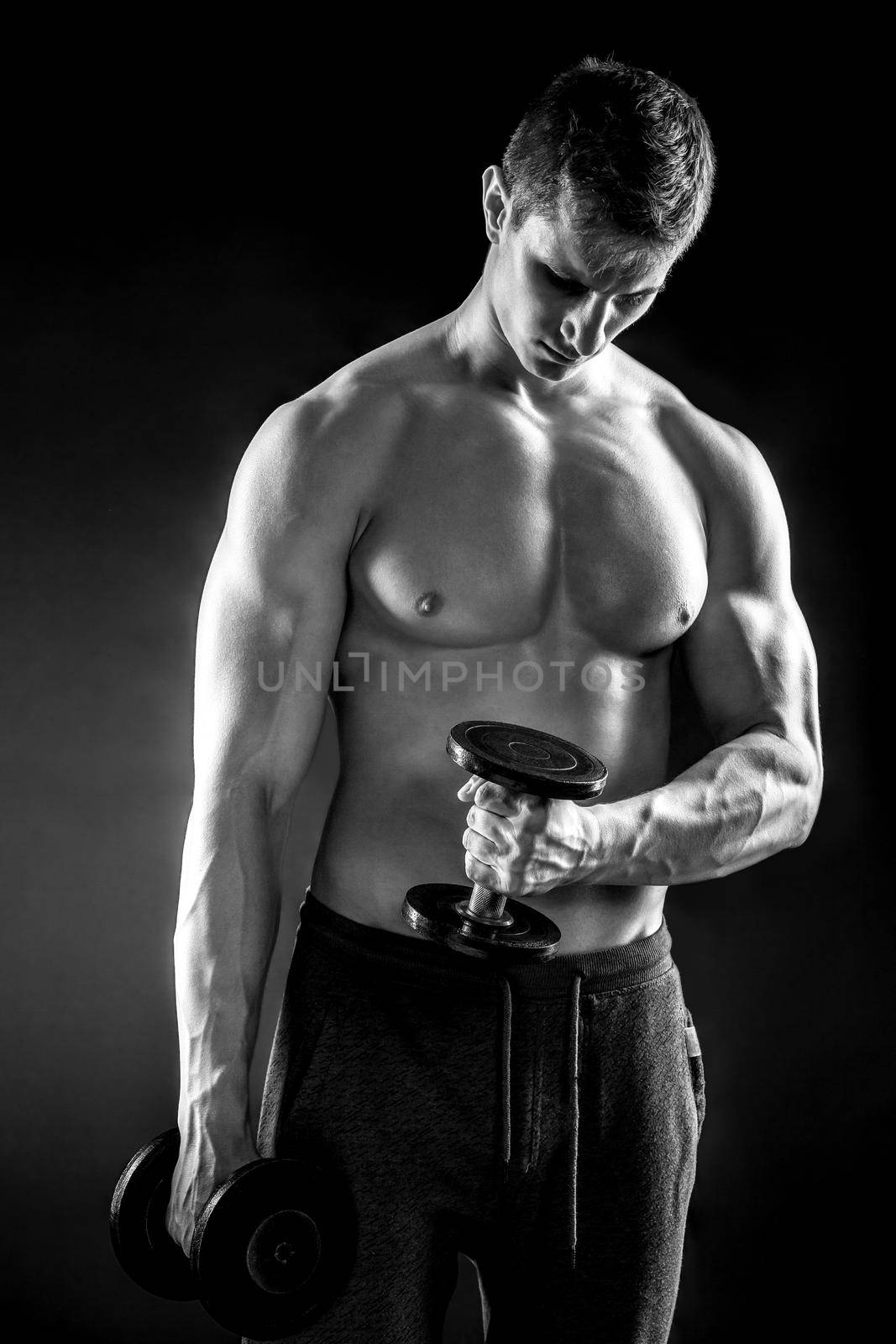 Mighty fitness man showing his gread body with dumbbells in hand on black background.. Black and white