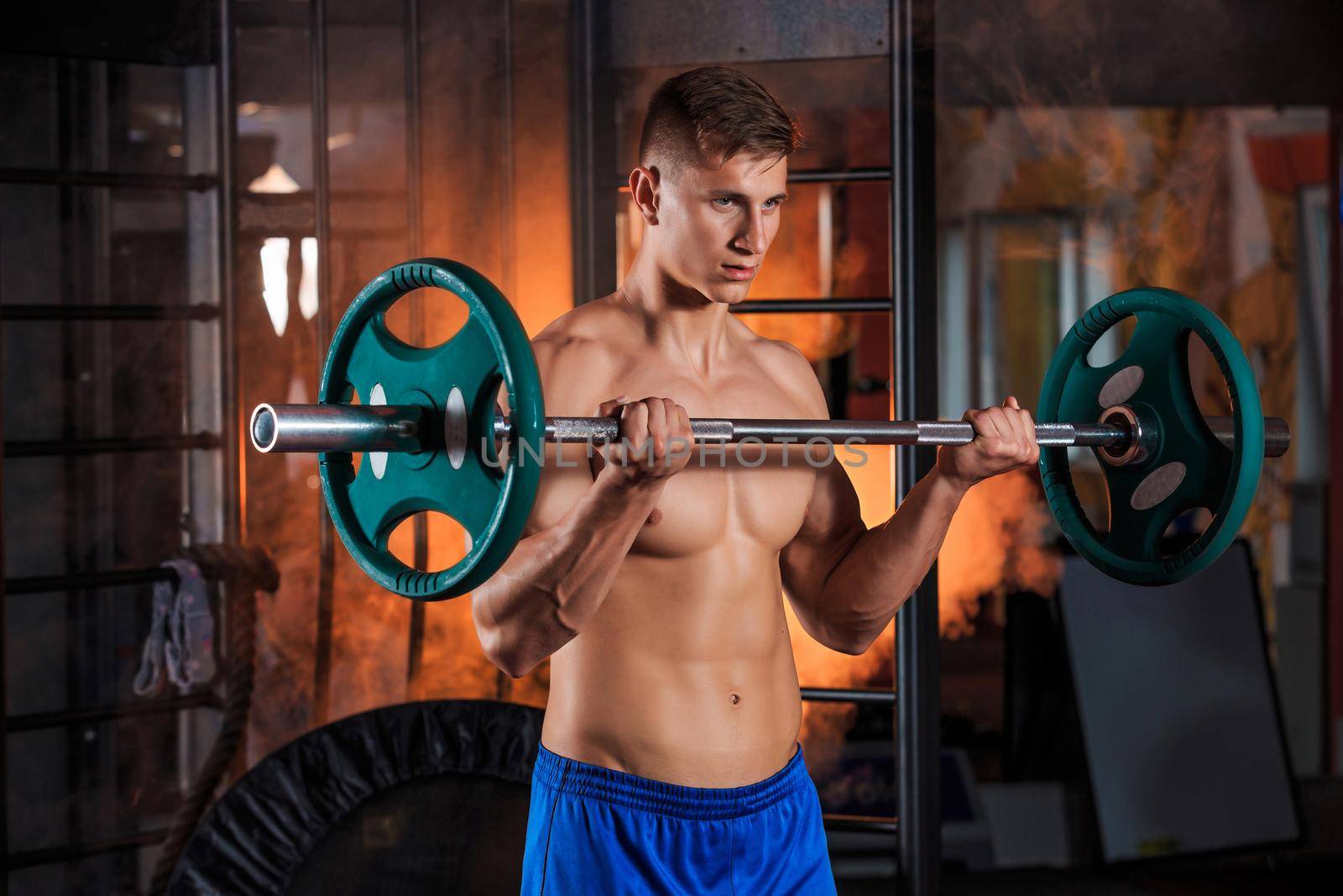 young man doing exercises with barbell in gym. Orange smoke on background
