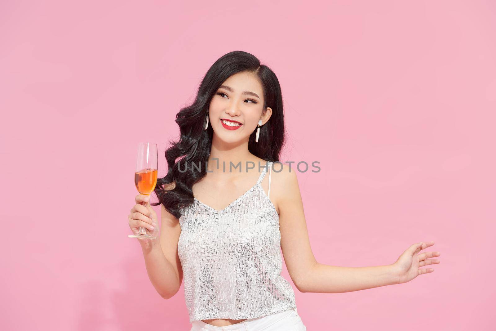 Good-looking asian girl in stylish attire standing in confident pose with wineglass on pink background. 