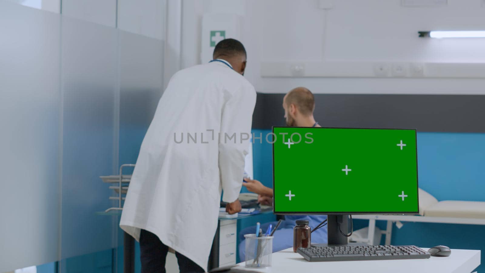 Mock up green screen chroma key computer with isolated display standing on desk in hospital office. Multi-ethnic team of discussing ill symptoms analyzing medical document. Medicine concept