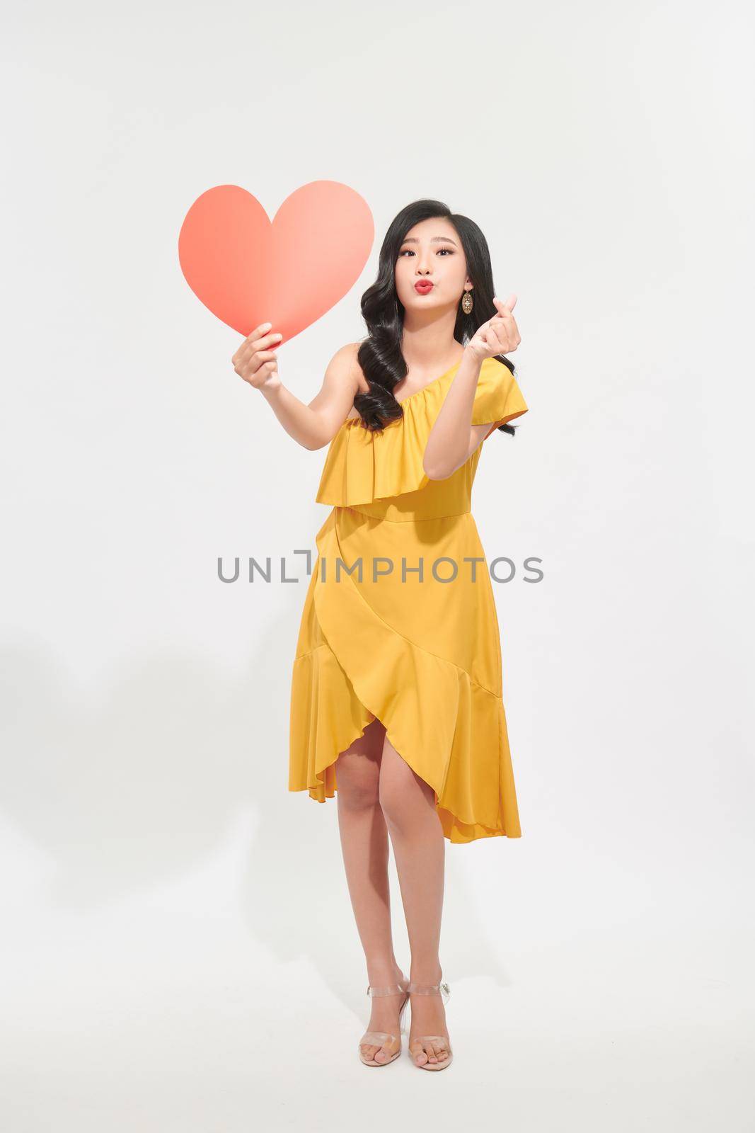 dreamy girl holding in hands big paper heart sending air kiss isolated on bright  color background by makidotvn