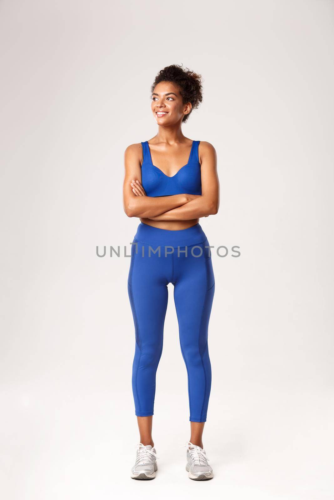 Full length of strong attractive african american sportswoman in sports bra and leggings, looking left and smiling at something, standing over white background, ready to workout.