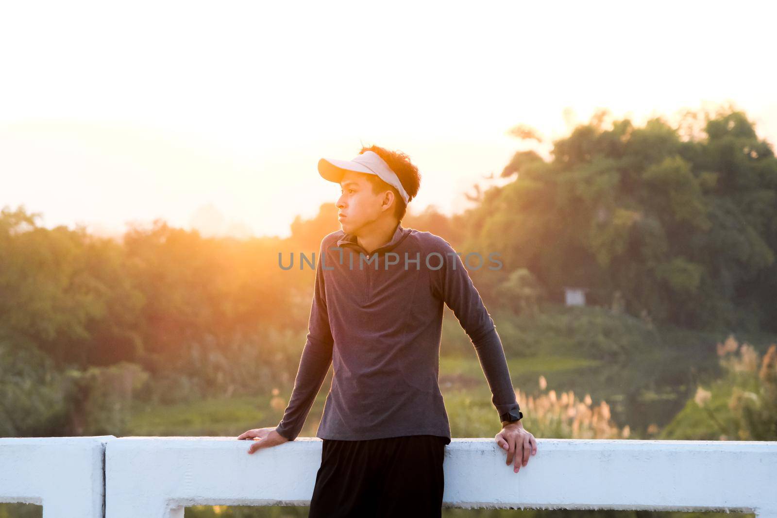 A healthy teenage boy resting on a bridge after jogging in the morning. Young man exercising outdoors. by TEERASAK