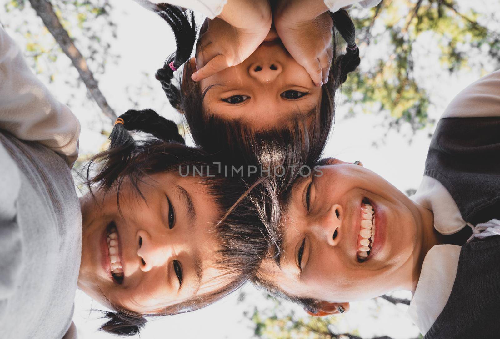 Two cute little Asian girls in summer outfits, having fun with a beautiful young mother smiling happily in the park. Motherhood and family concept.