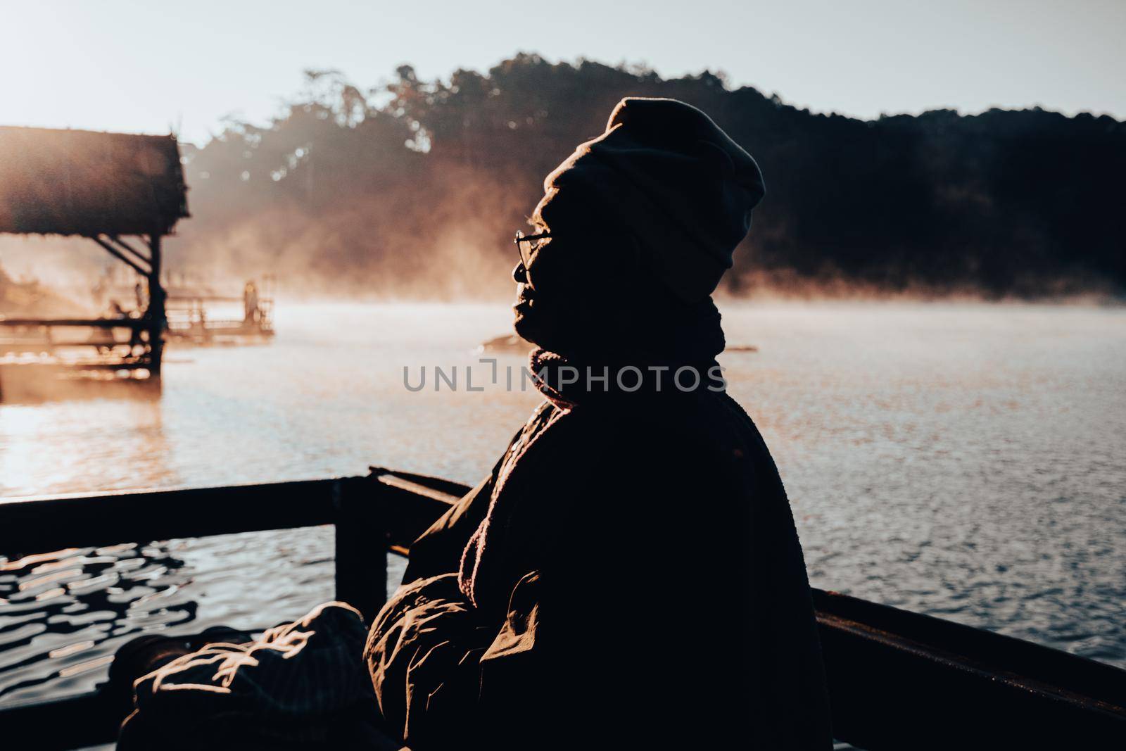 An Asian senior man enjoying the nature and the warm morning sun by the lake in winter. Elderly man relaxing in the park . Outdoor leisure lifestyle of the elderly.
