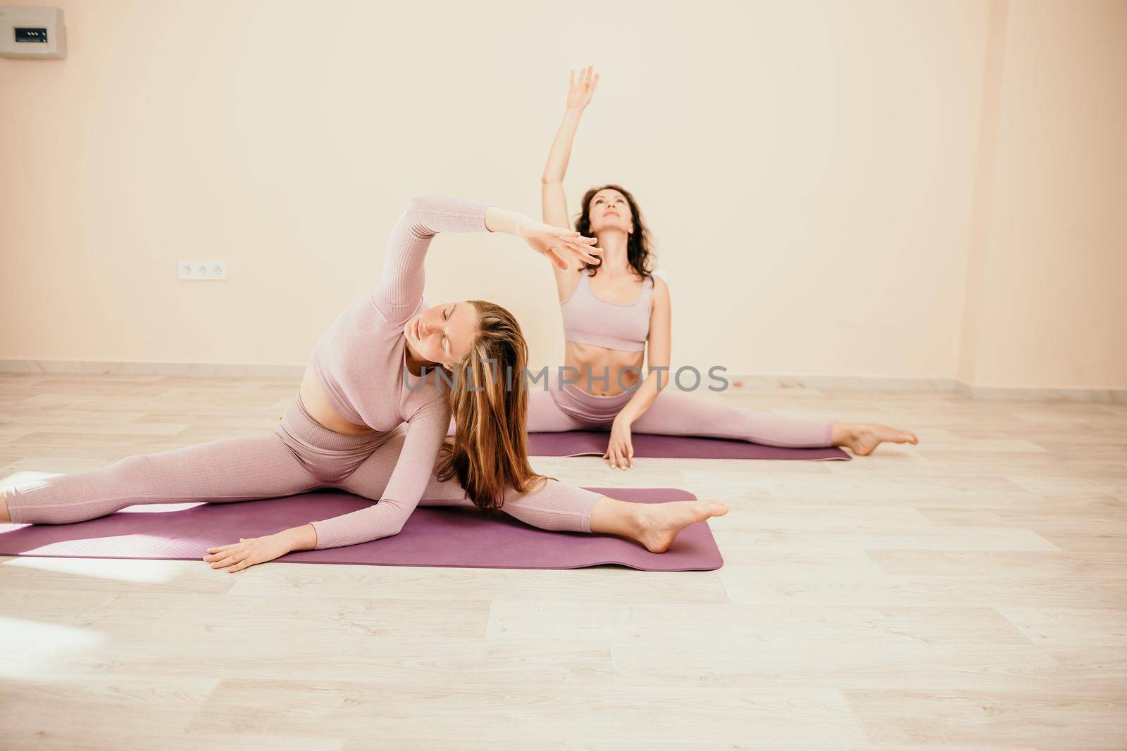 Well looking middle aged sporty woman, fitness instructor in pink sportswear doing stretching and pilates on yoga mat in the studio with mirror. Female fitness yoga. Healthy lifestyle and harmony. by panophotograph