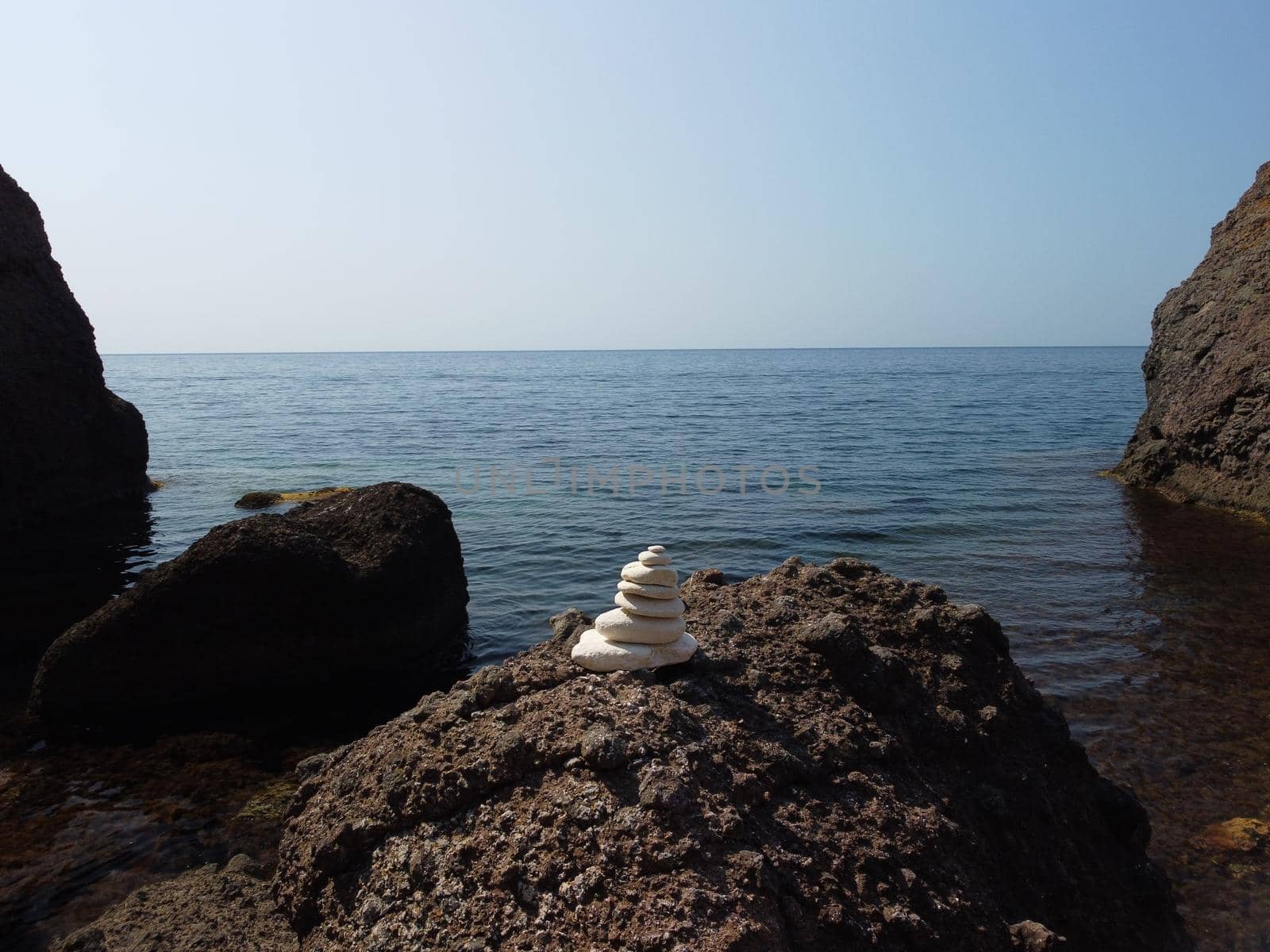 Pyramid stones on the seashore with warm sunset on the sea background. Happy holidays. Pebble beach, calm sea, travel destination. Concept of happy vacation on the sea, meditation, spa, calmness.