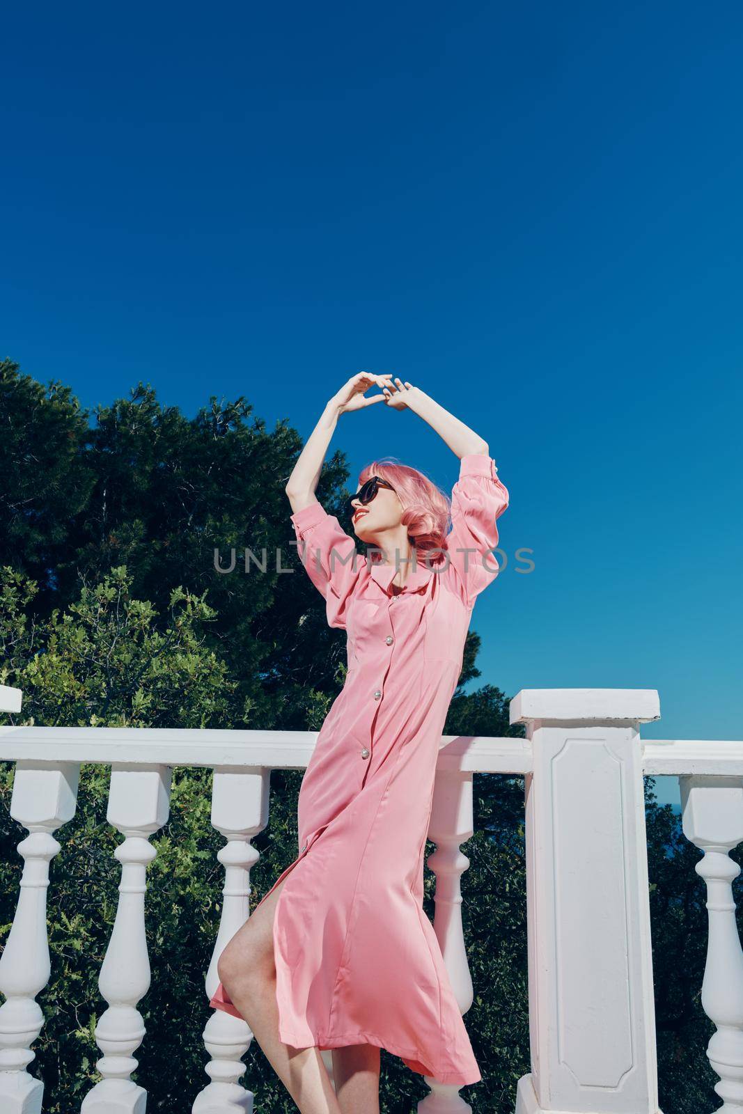 glamorous woman pink dress modern style stands near the railing sunny day. High quality photo
