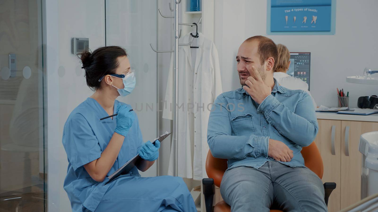 Dentistry nurse taking notes and talking to patient about toothache at oral care clinic. Woman assistant consulting man in pain with denture problems, discussing about dental procedure.