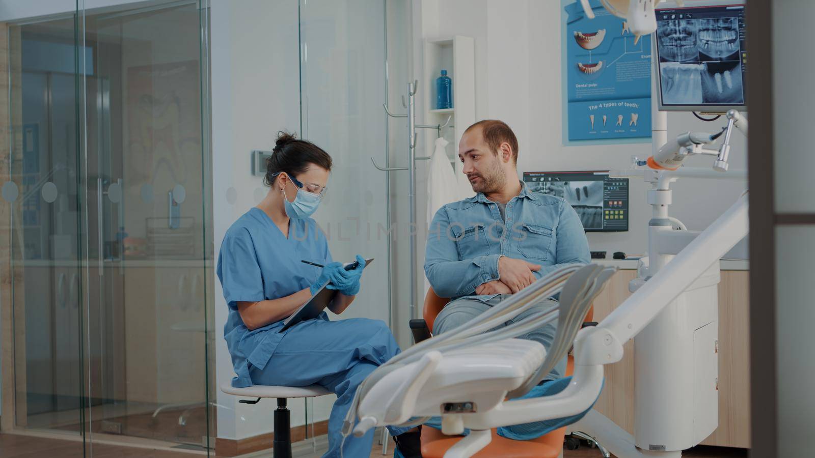 Dental nurse taking notes and consulting patient with toothache, preparing to do oral care examination with dentistry tools. Man attending dental checkup appointment with stomatologist
