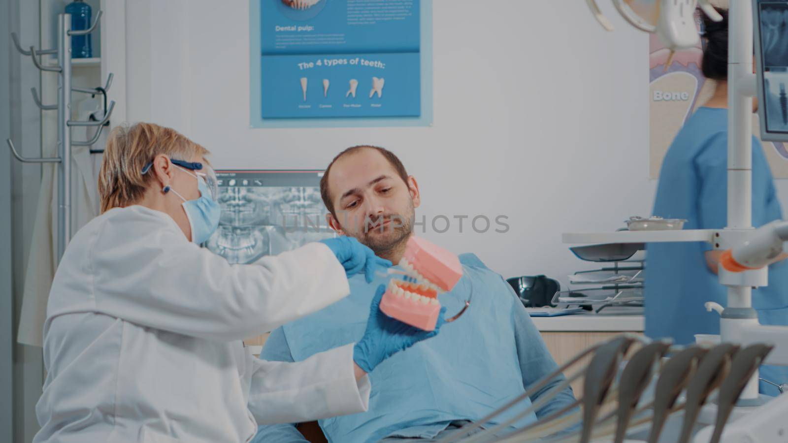 Stomatologist using artificial jaw to explain correct way to brush teeth, doing oral care lesson with patient. Dentist teaching man to use toothbrush to prevent caries and toothache. Teach hygiene