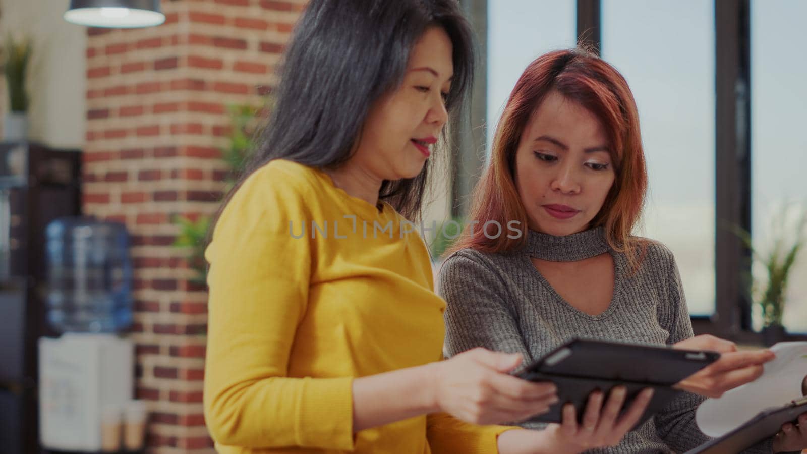 Team of asian women analyzing tablet and paperwork to create financial presentation for company development. Creative people doing teamwork on career project and marketing application.